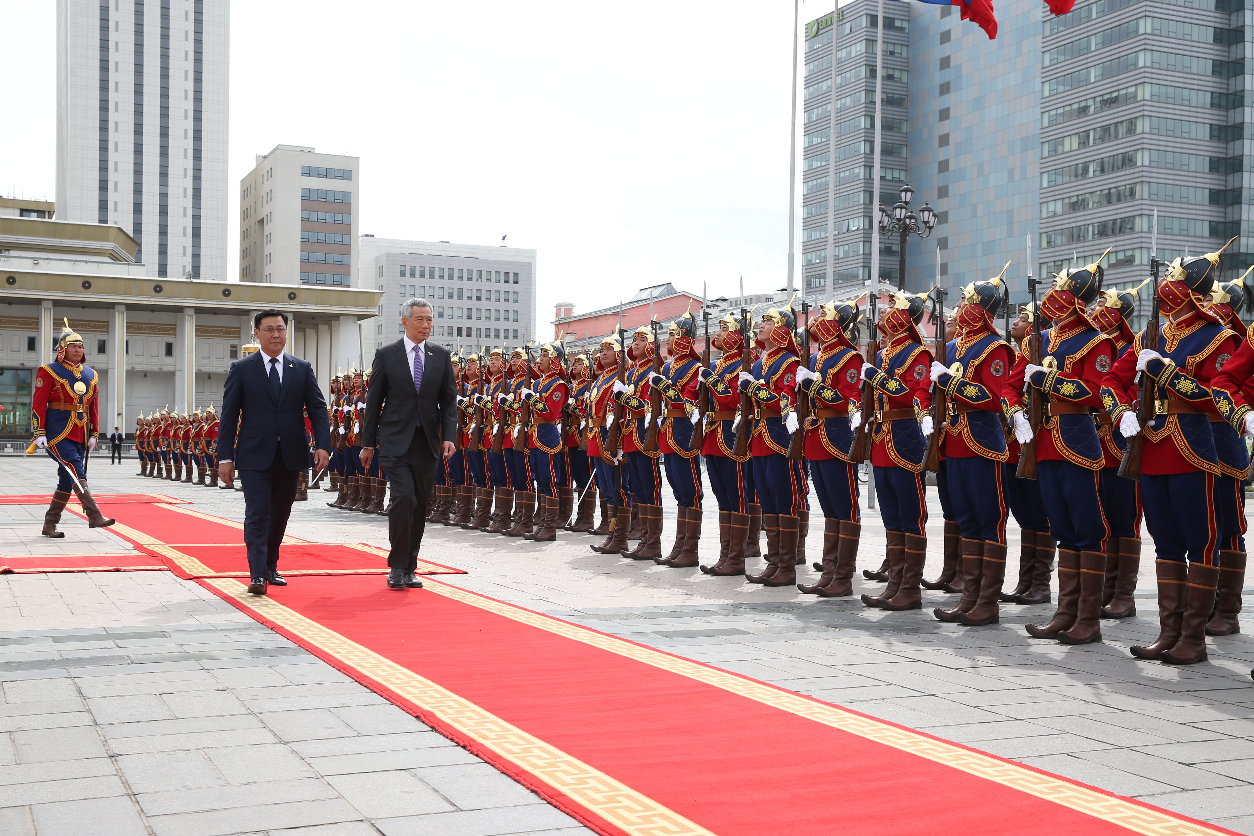 Two men in suits walk a red carpet past a line of soldiers in ceremonial dress.