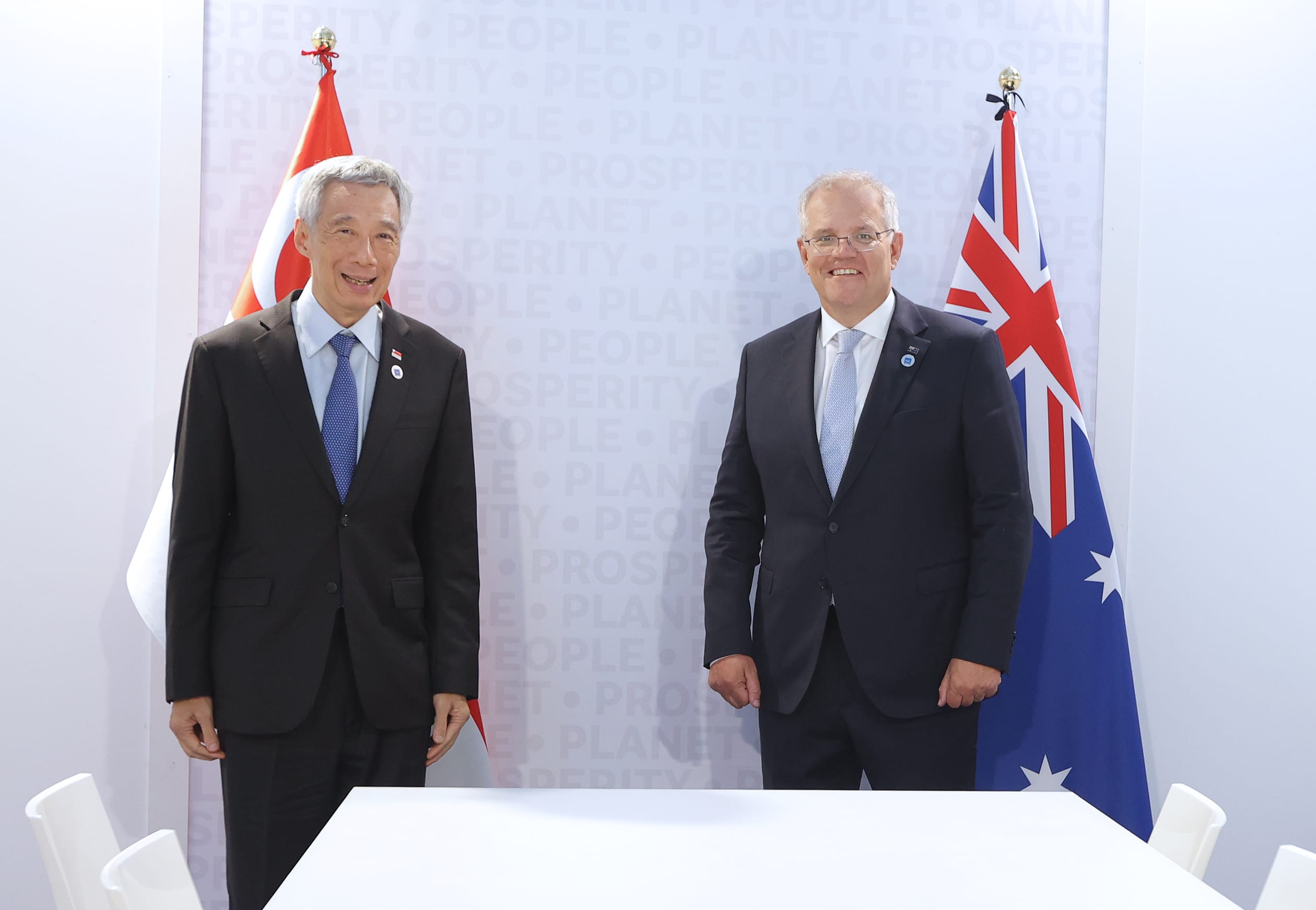 Lee Hsien Loong & Scott Morrison, in suits, stand before Singaporean & Australian flags.