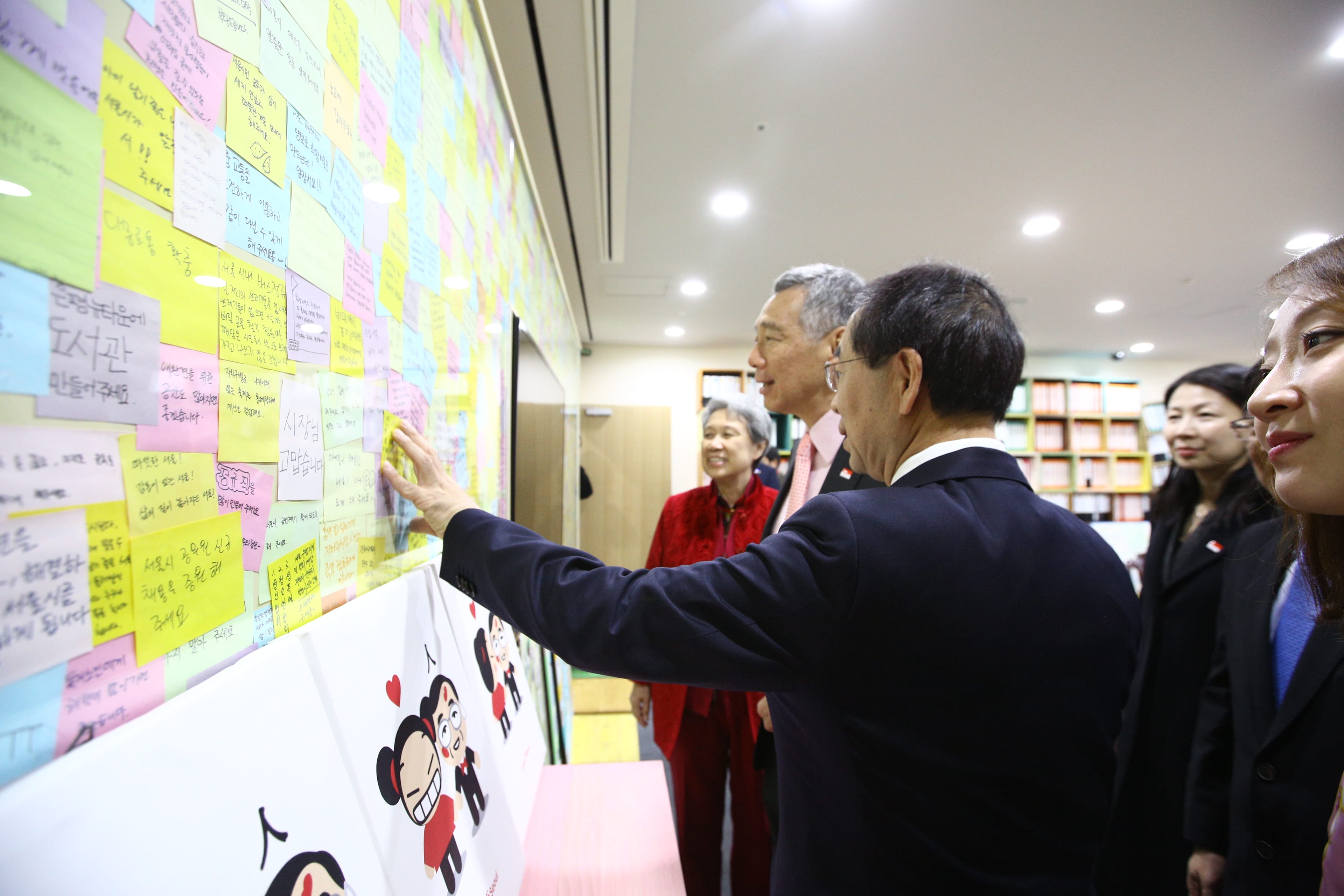 Group looking at a wall of colorful sticky notes, with illustrations of Pucca characters below.