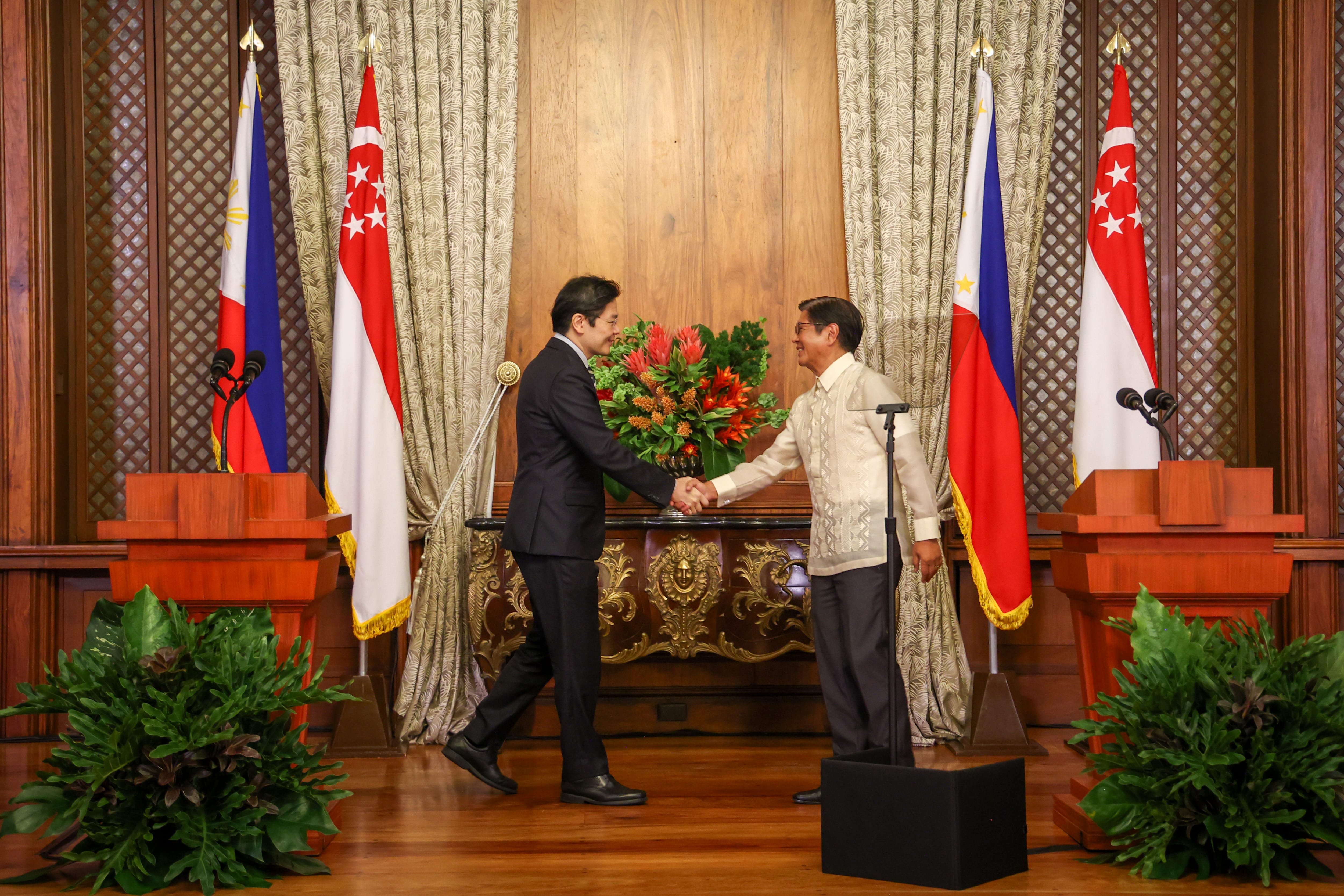 Two men shake hands before flags of the Philippines and Singapore.