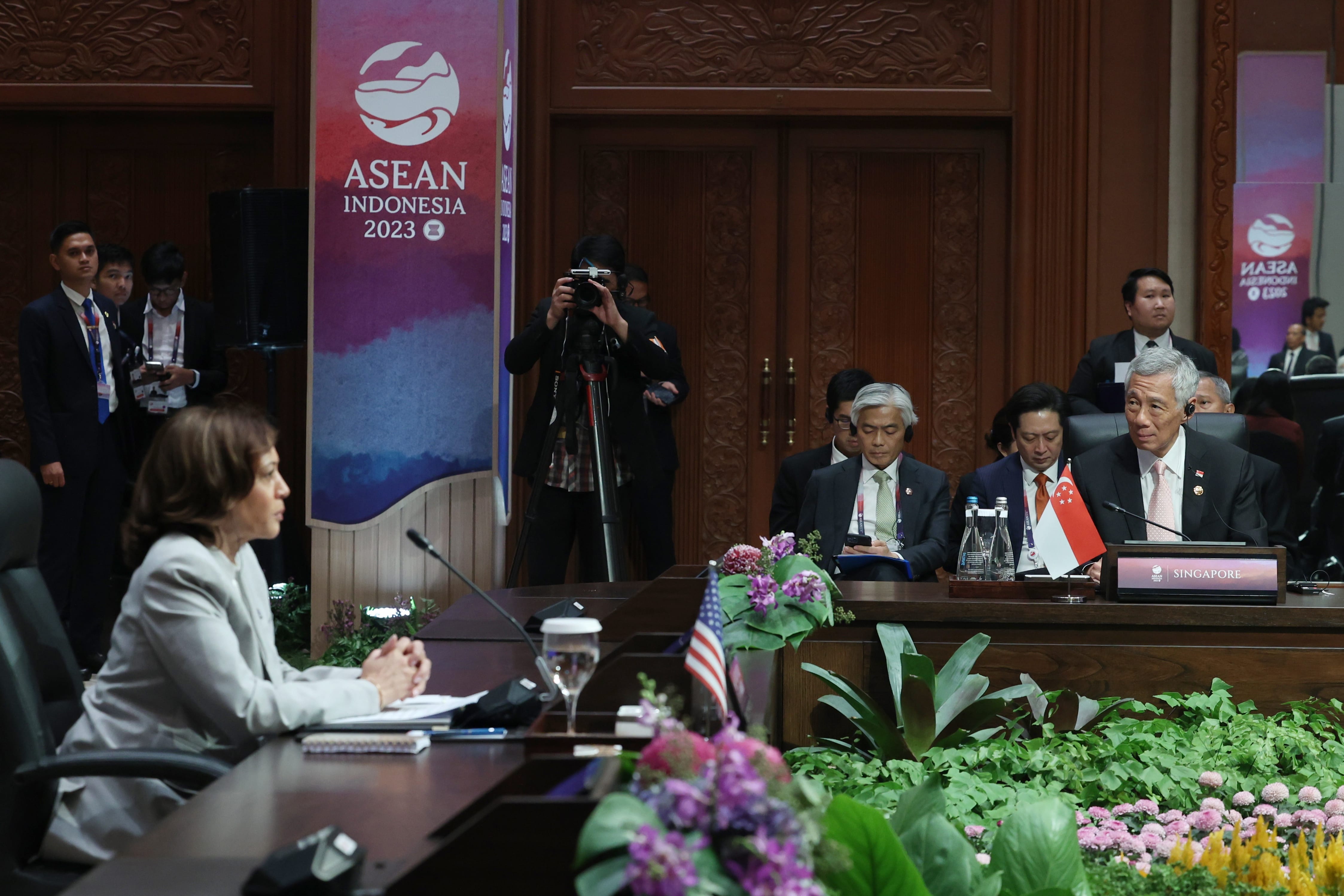 World leaders at ASEAN summit behind table with Singapore flag; photographer visible.