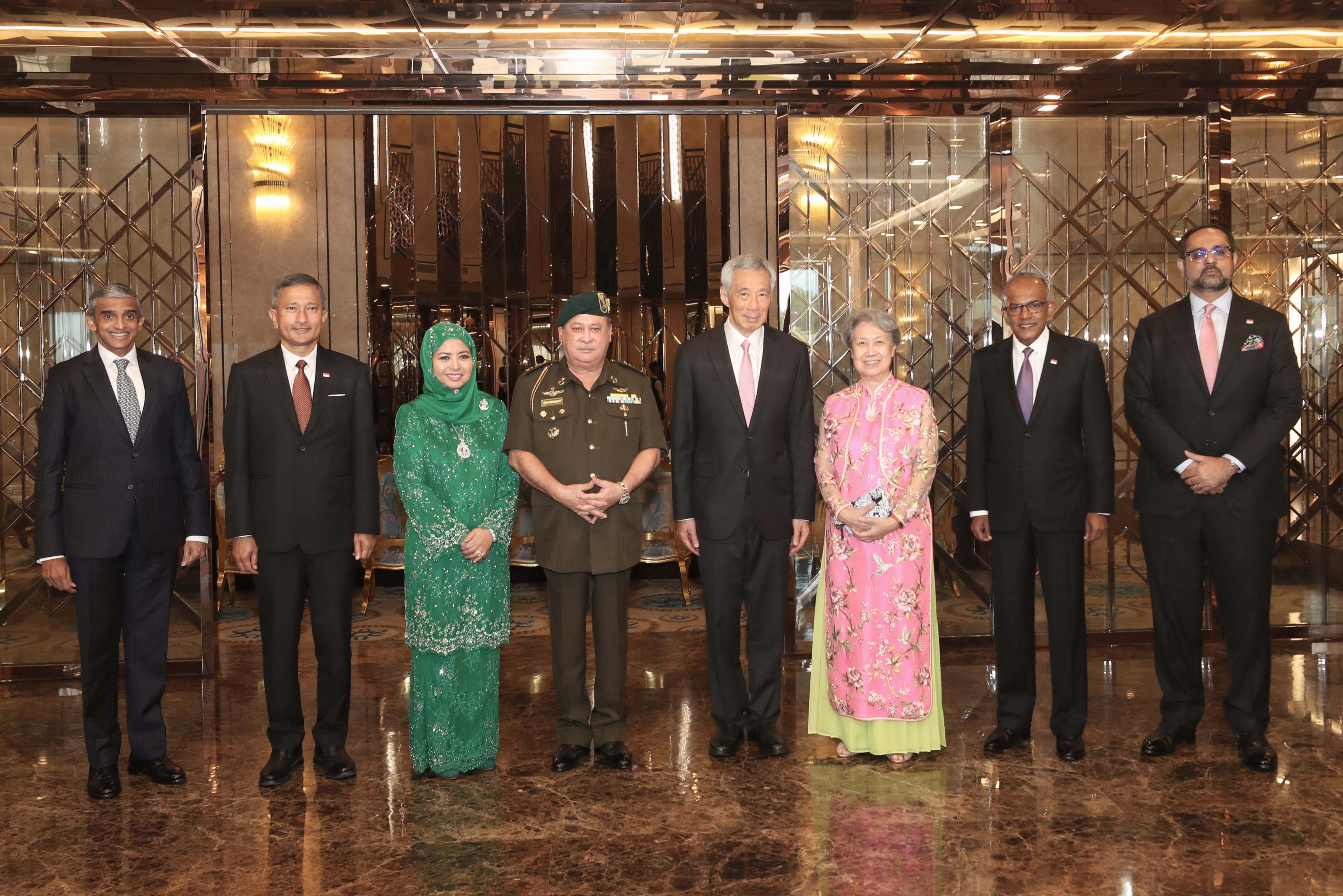 Group of eight people in formal wear and military attire posed in front of a paneled mirror.