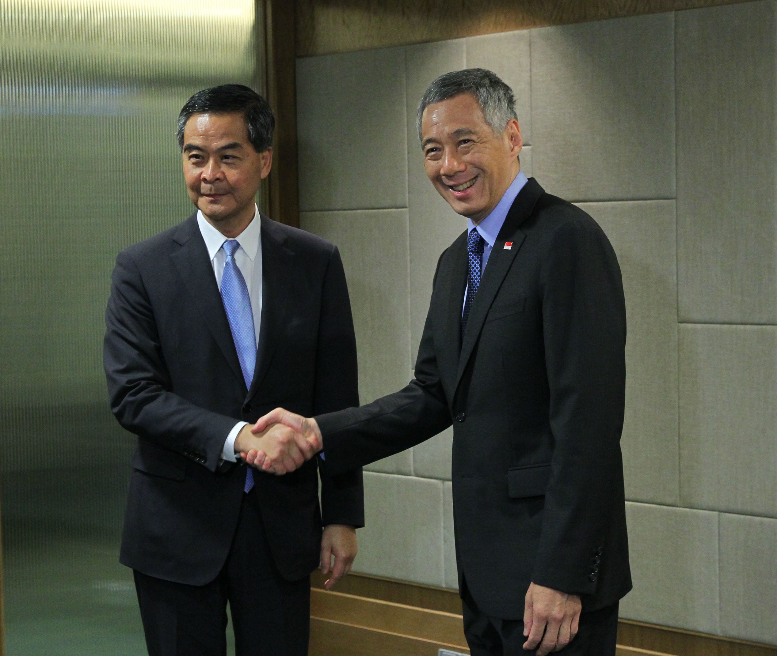 Two men in suits shaking hands in front of a wall.