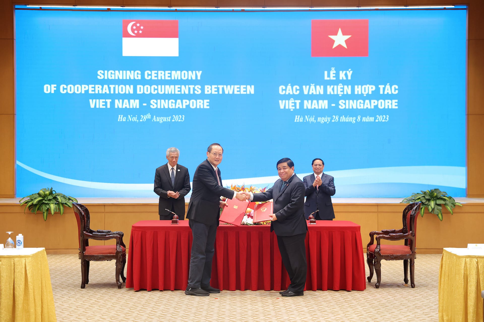 Two men shaking hands with Singapore and Vietnam flags in the background.