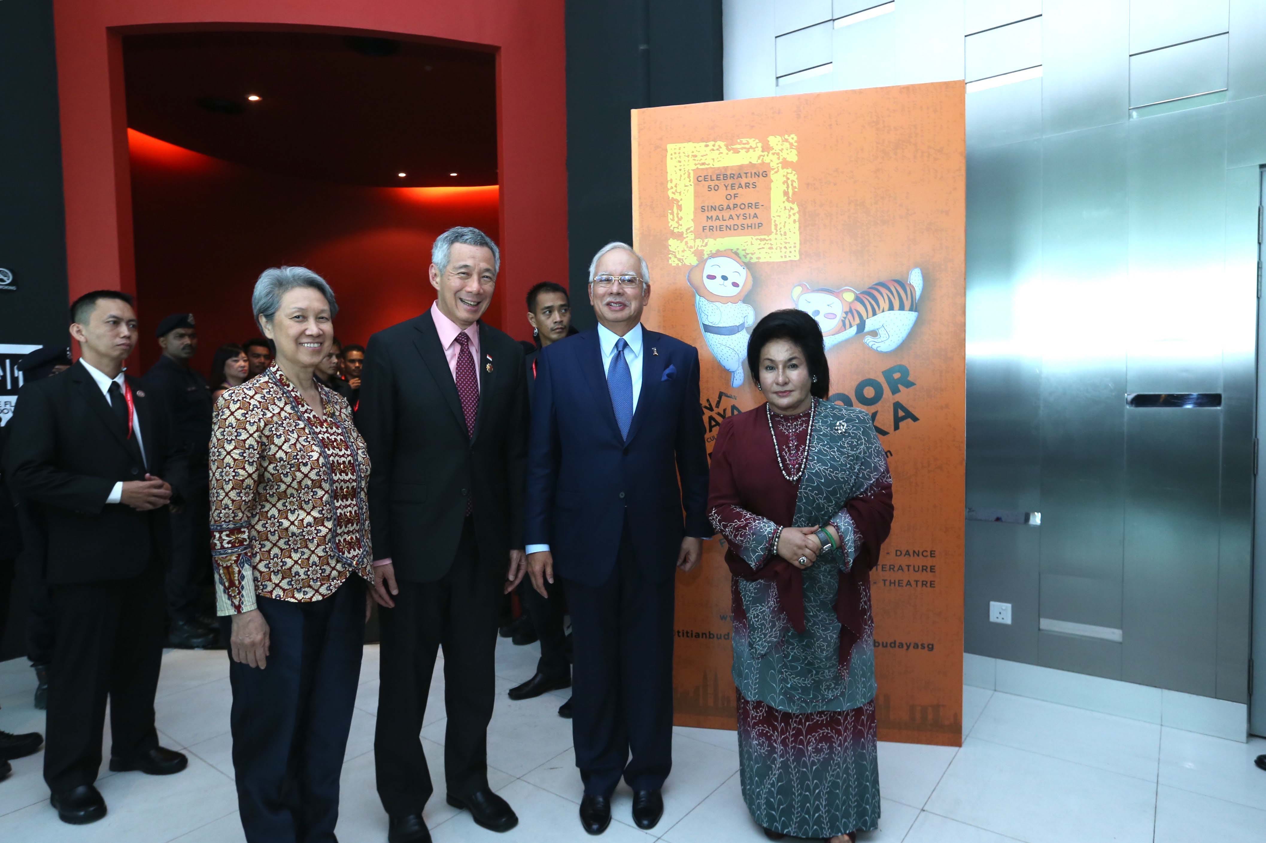 Four people pose next to a sign reading "Celebrating 50 Years of Singapore-Malaysia Friendship."