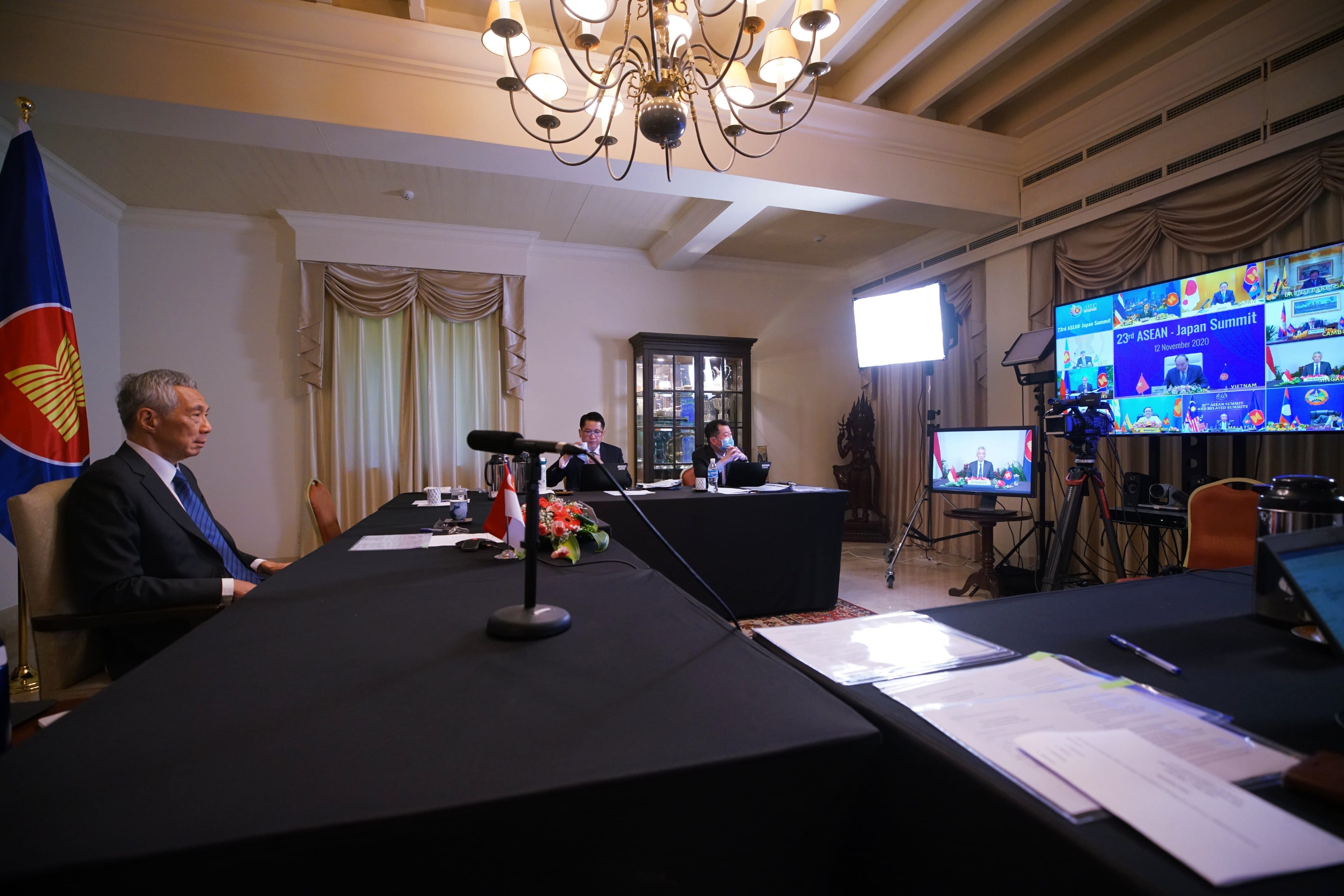 Meeting room with Lee Hsien Loong at table, ASEAN flag, and video conference screens.