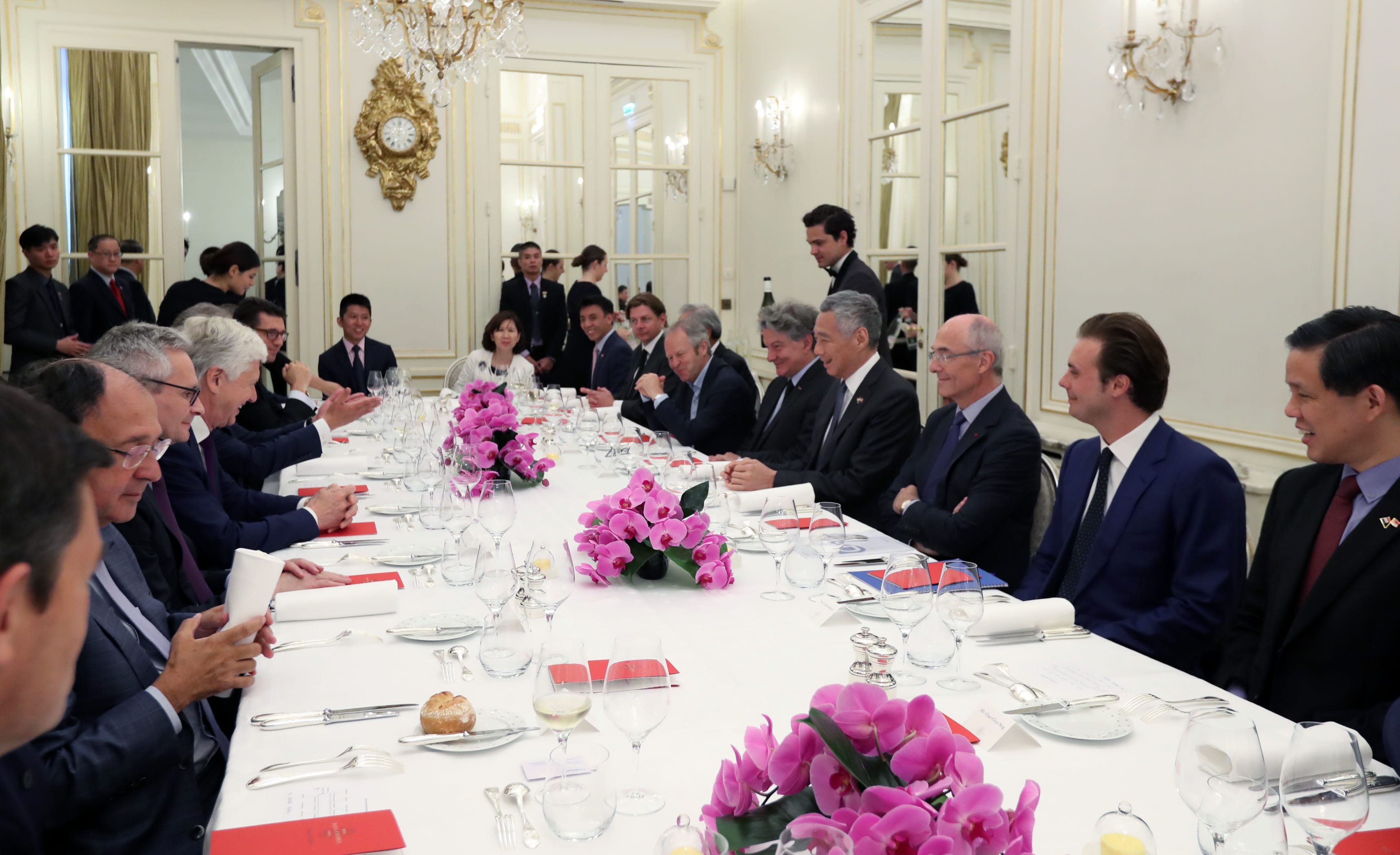 People seated at a long formal dinner table with pink orchid centerpieces.