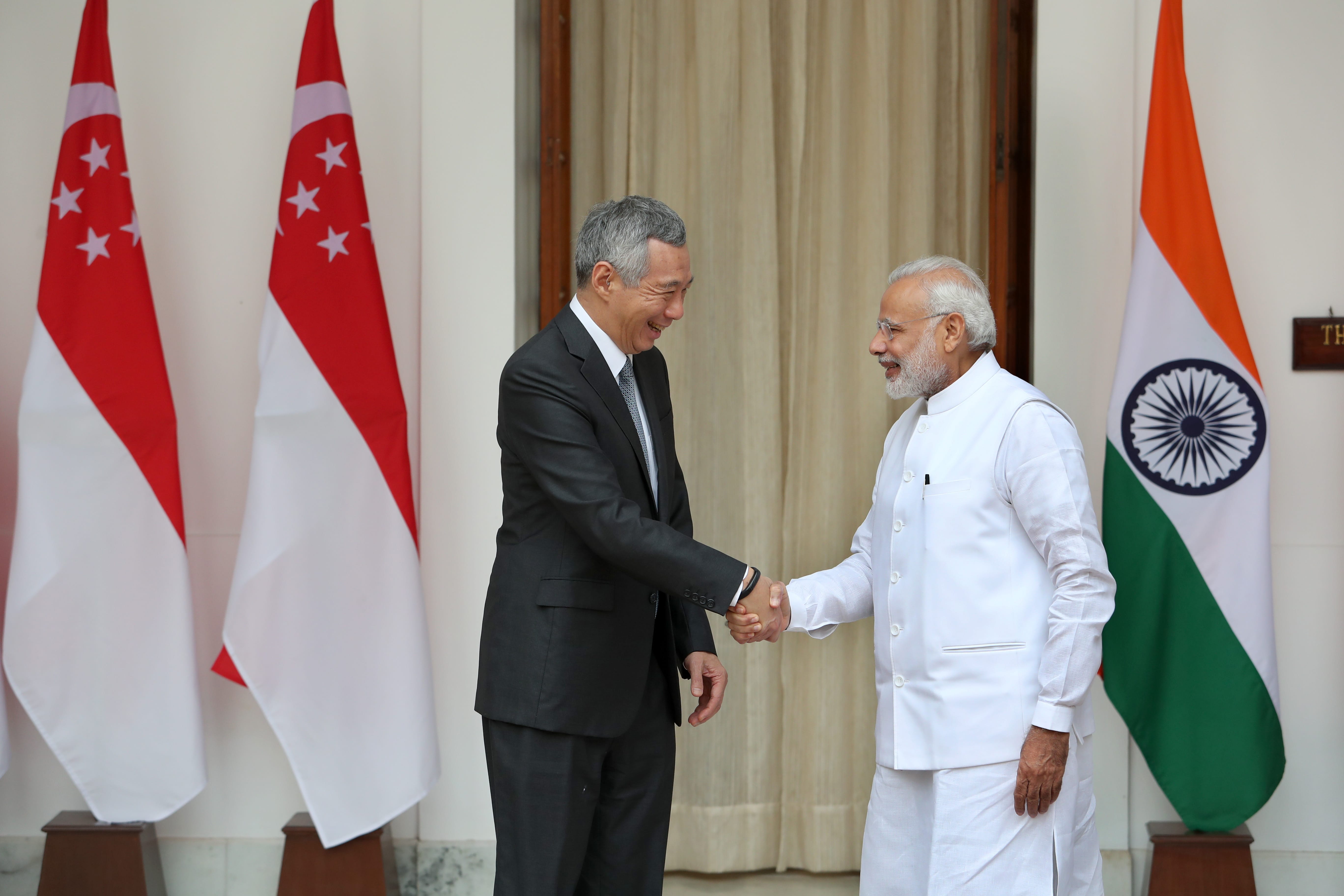 Lee Hsien Loong and Narendra Modi shaking hands by Singapore and India flags.