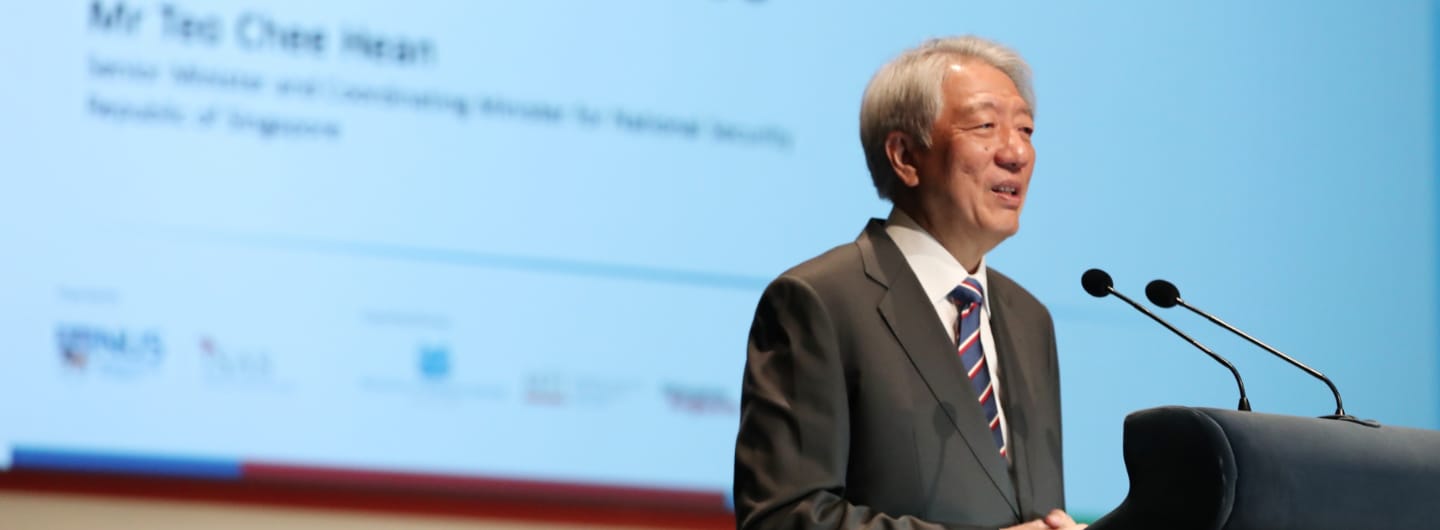 Mr. Teo Chee Hean at a podium with two microphones in front of a blue screen.