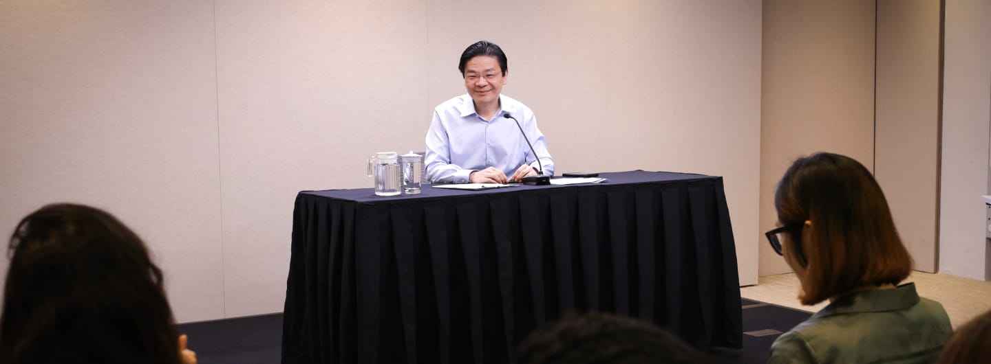 Heng Swee Keat sits behind a black covered table with a microphone, facing an audience.