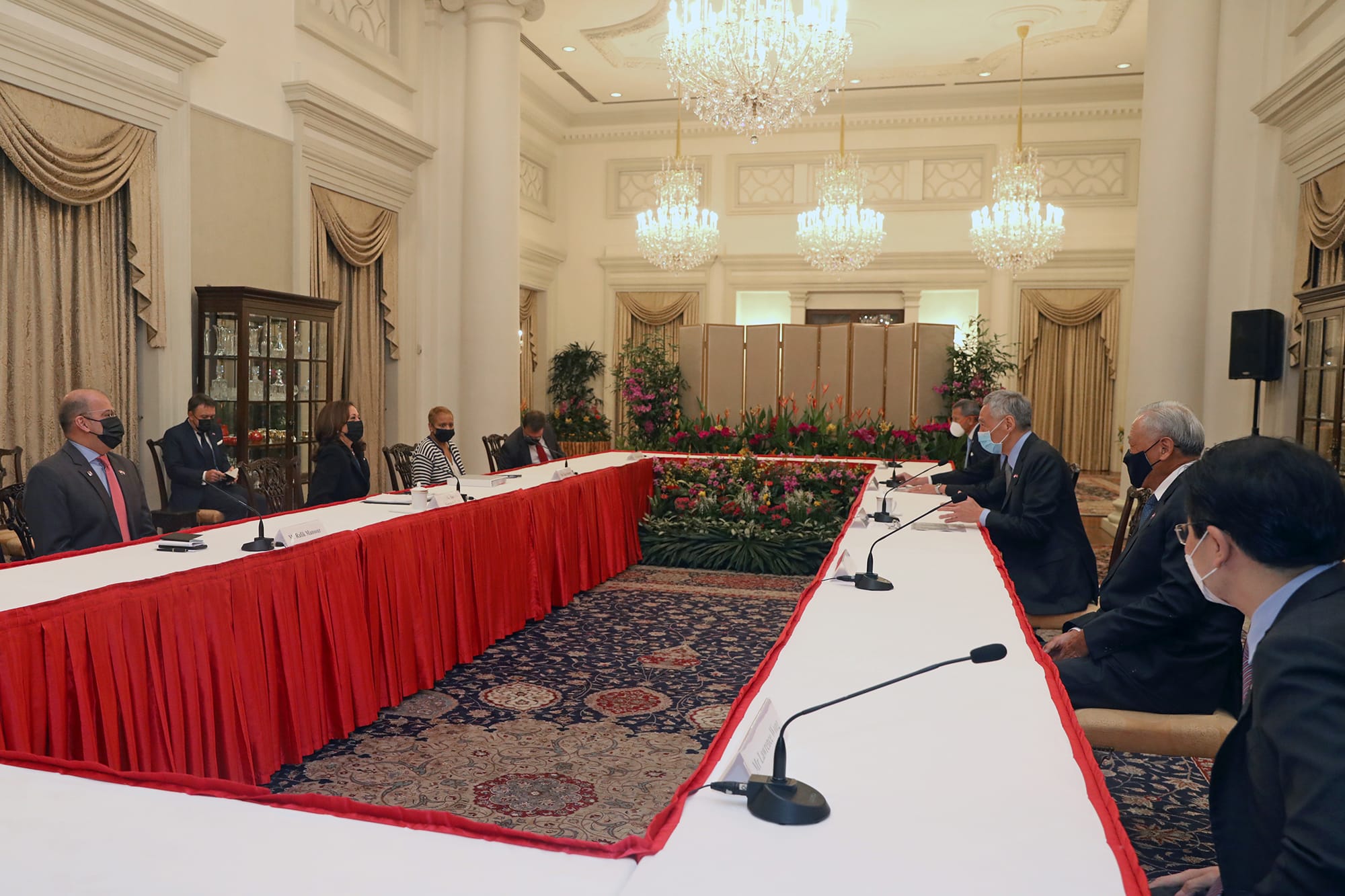 People in face masks at a long conference table in a formal room with chandeliers.