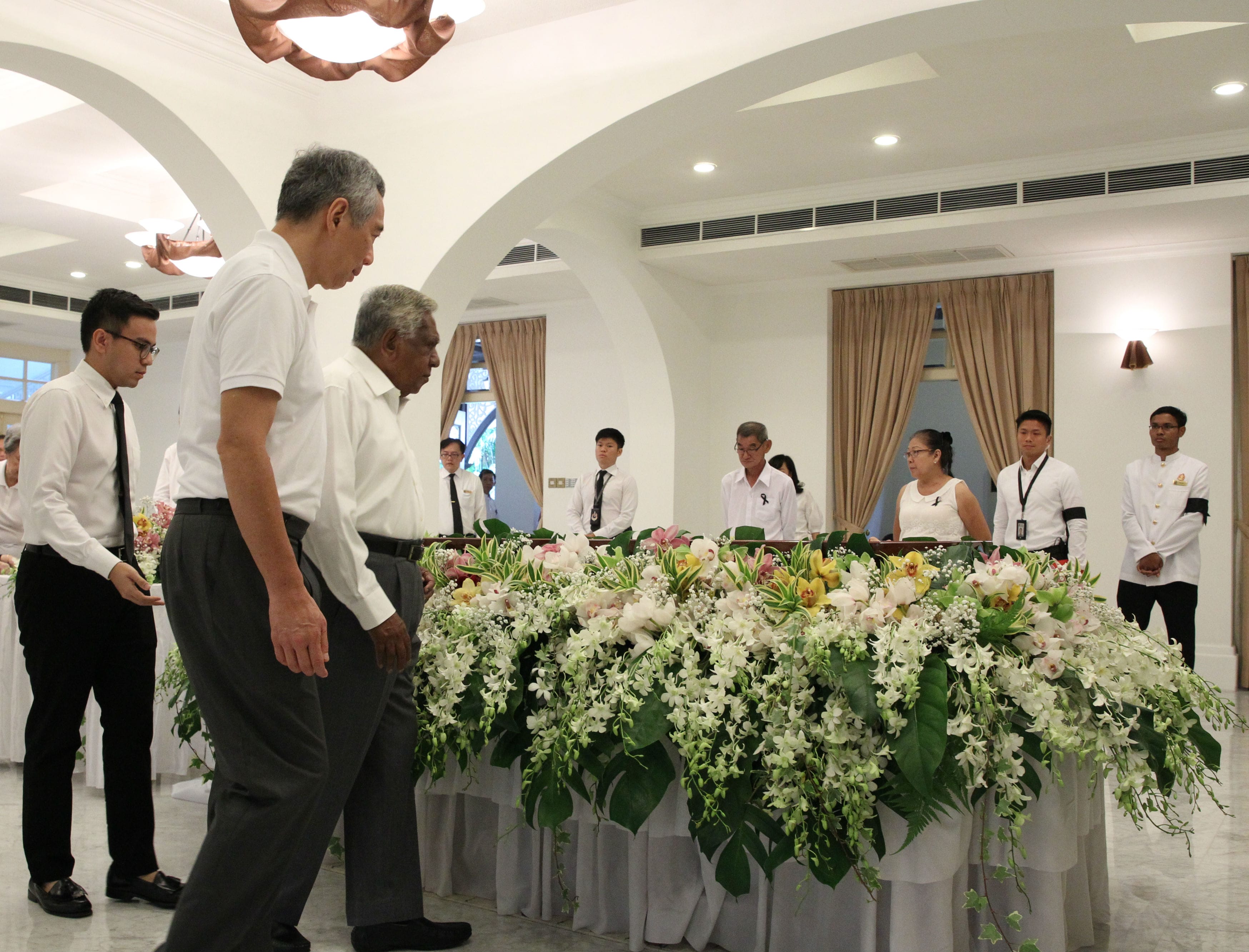 People filing past a large floral arrangement at a formal event.