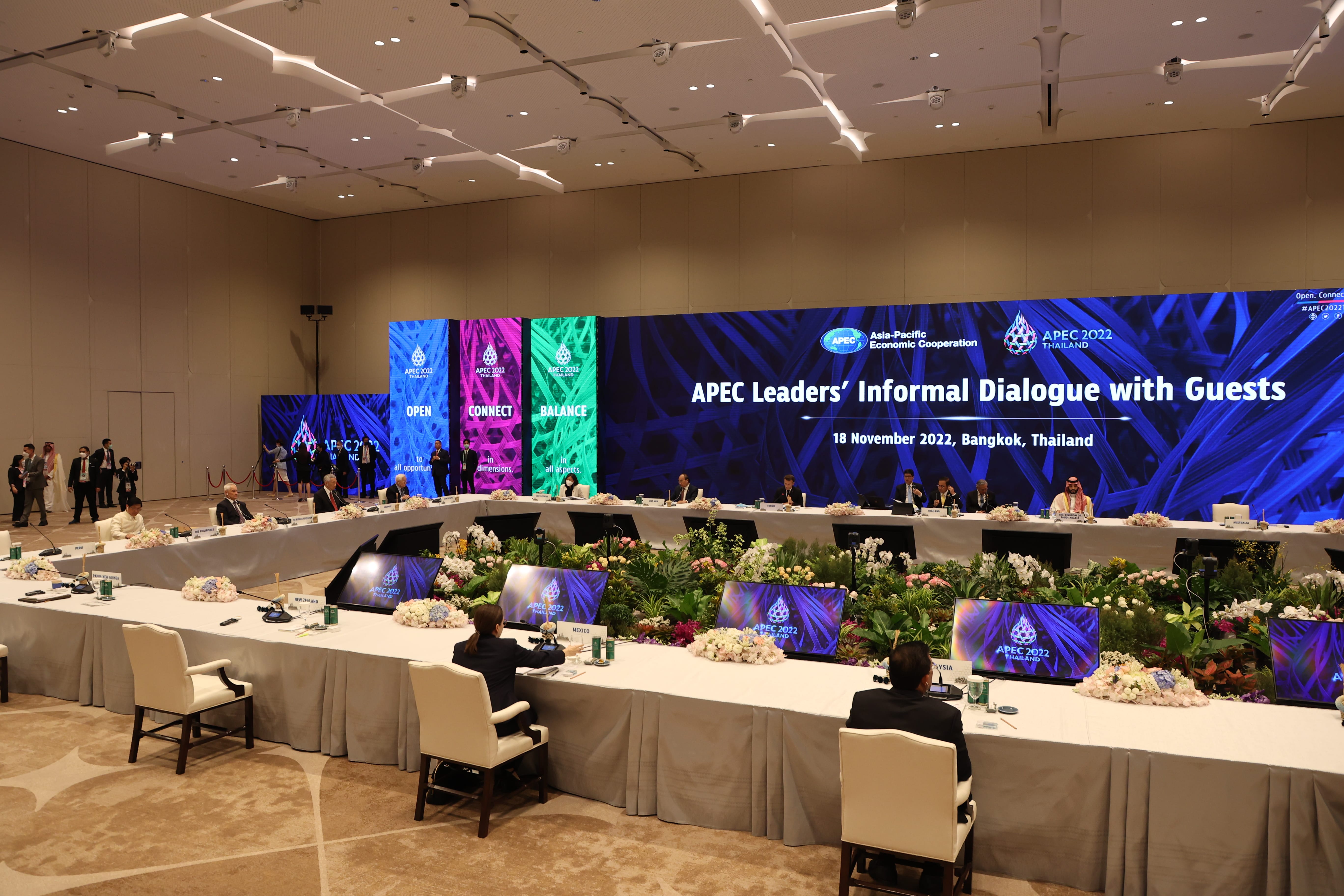 APEC leaders at long table in conference room, floral arrangements and APEC 2022 branding.