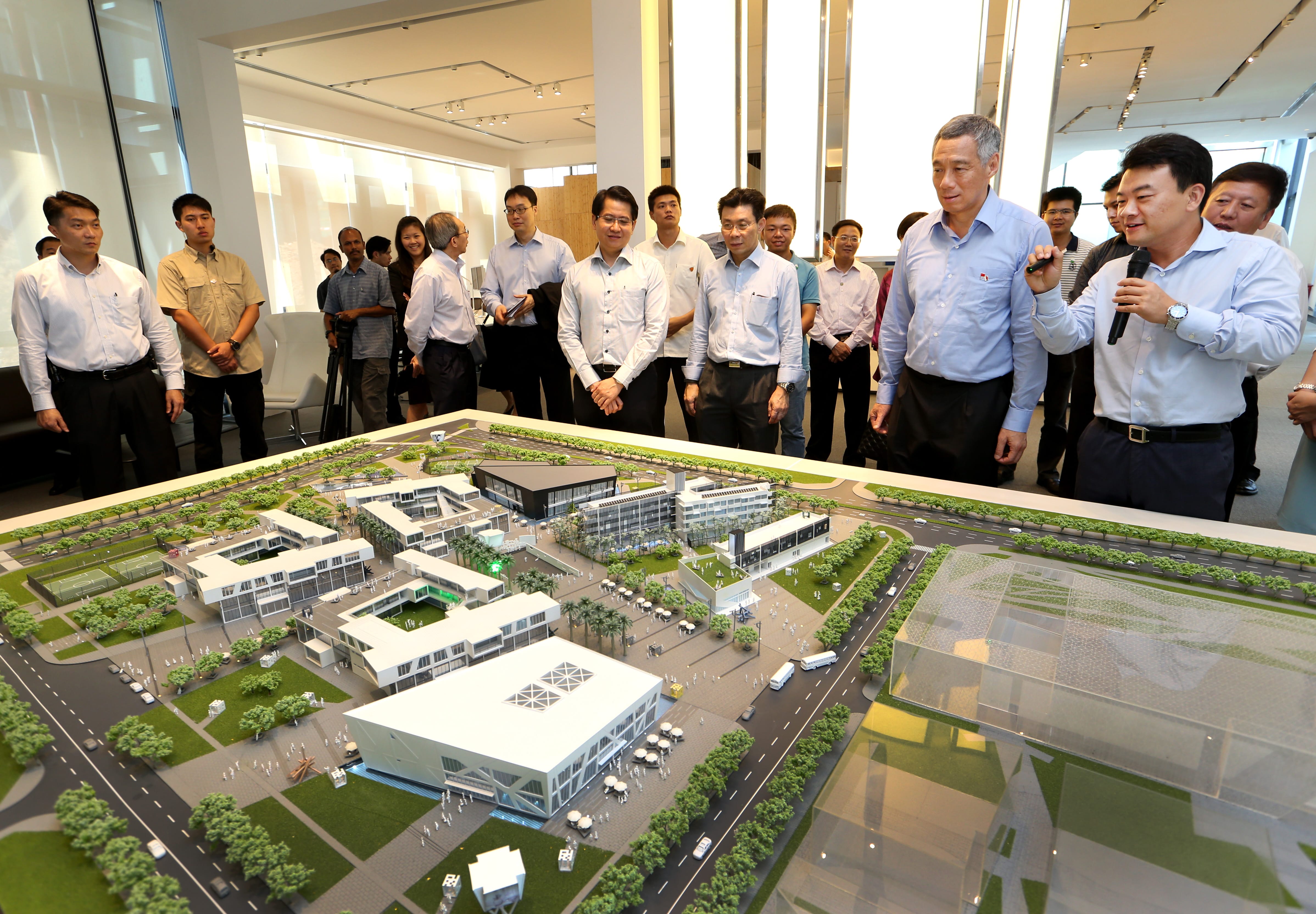 Group of people view an architectural model; one man speaks into a microphone.