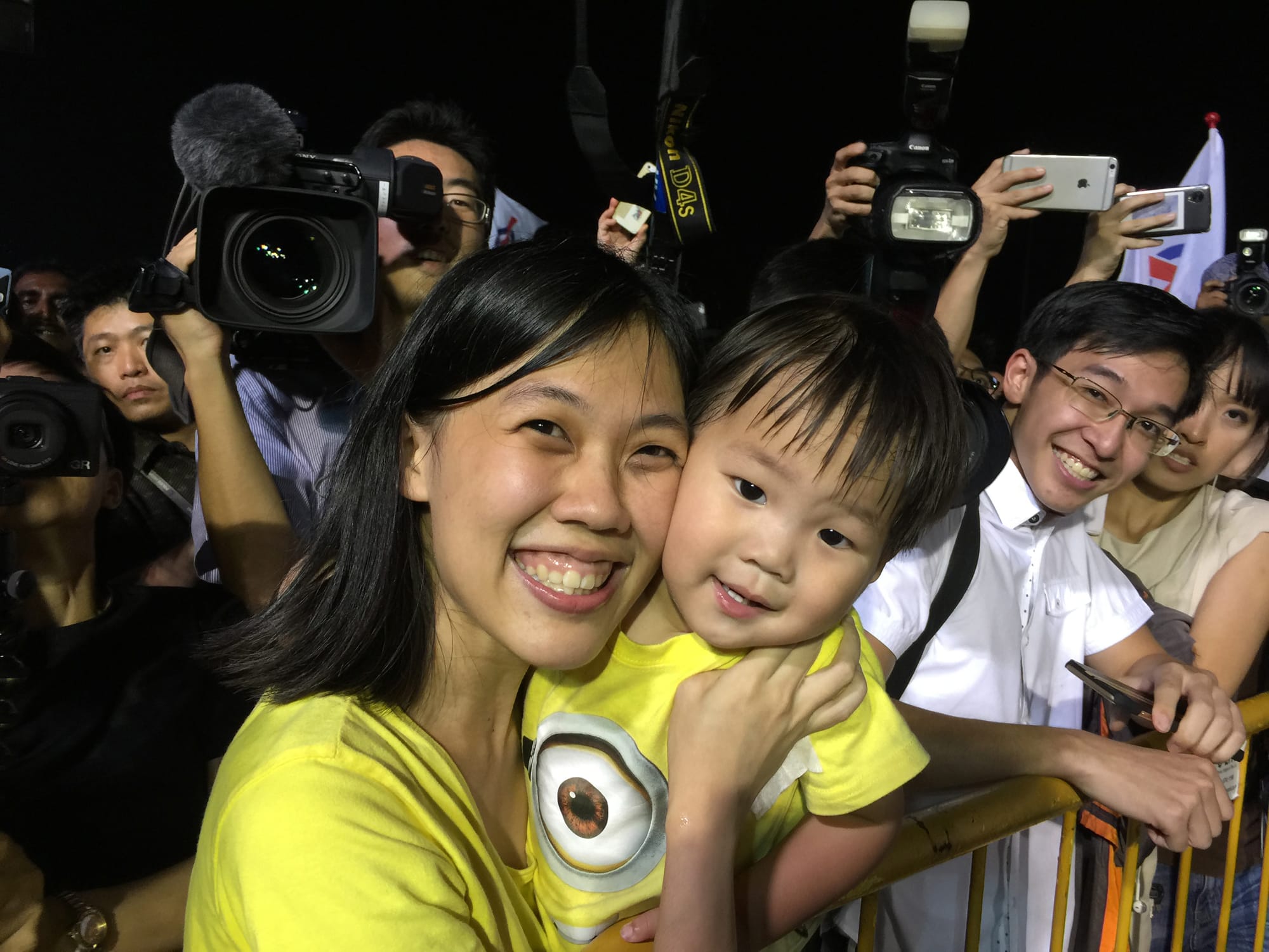Woman and child wearing a Minions t-shirt, surrounded by photographers with cameras.