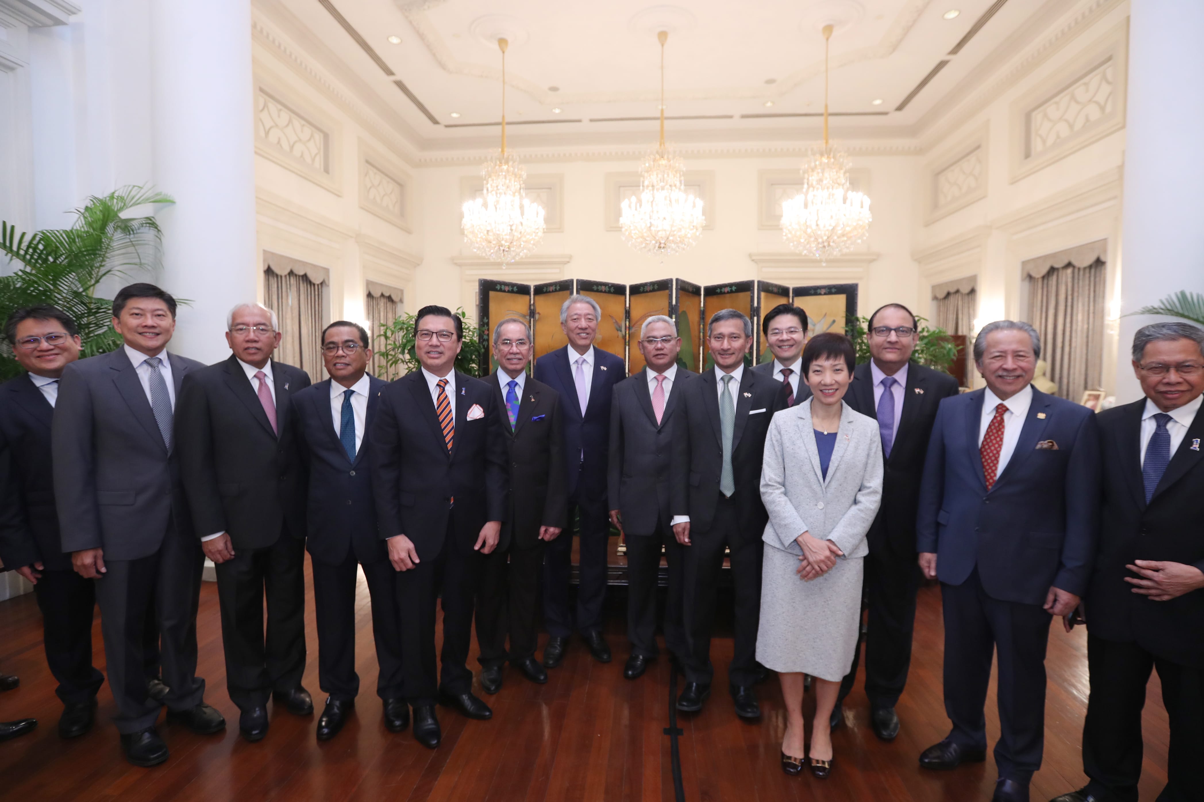 Group portrait of approximately 15 people in suits, standing in an ornate room.