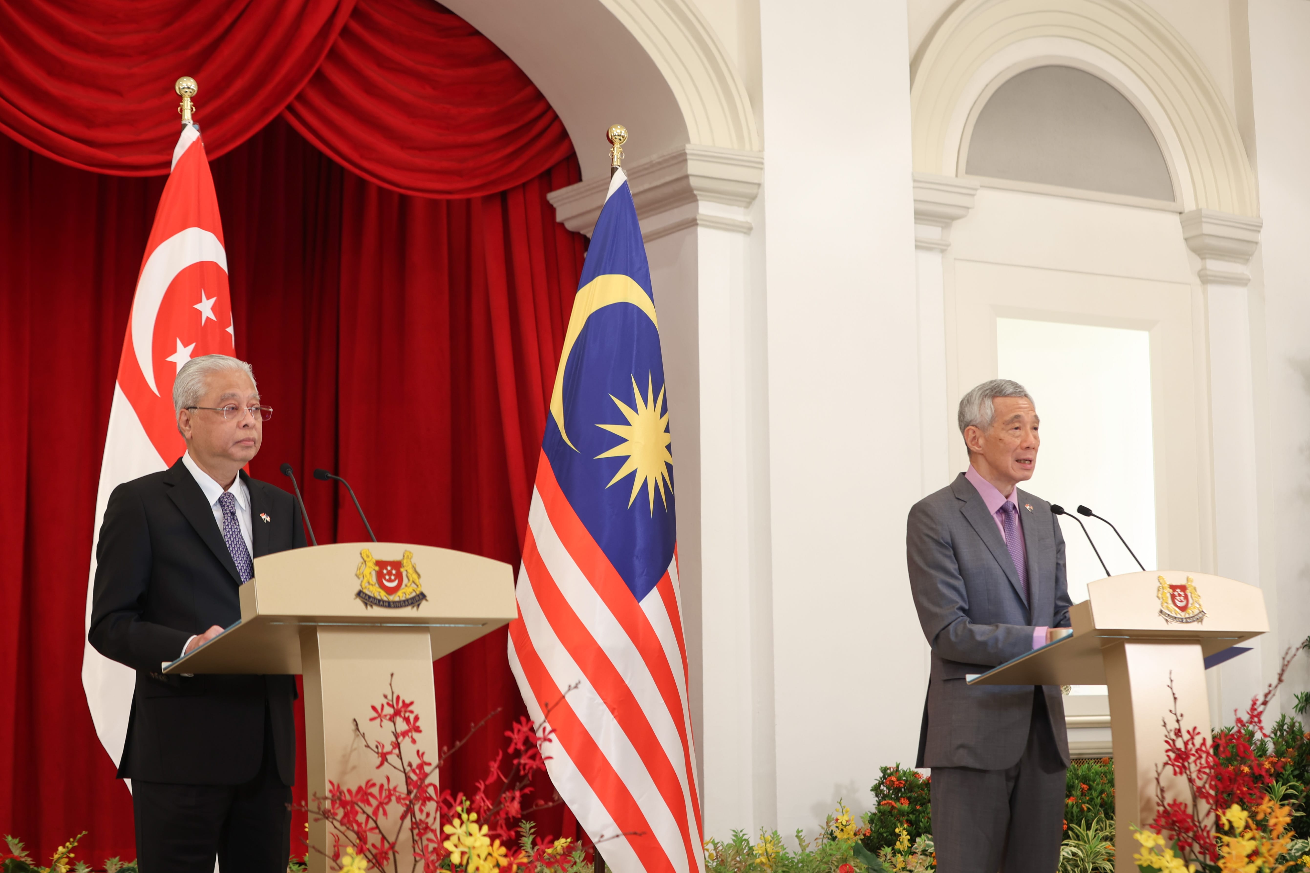 Lee Hsien Loong and Ismail Sabri Yaakob at podiums flanked by national flags.