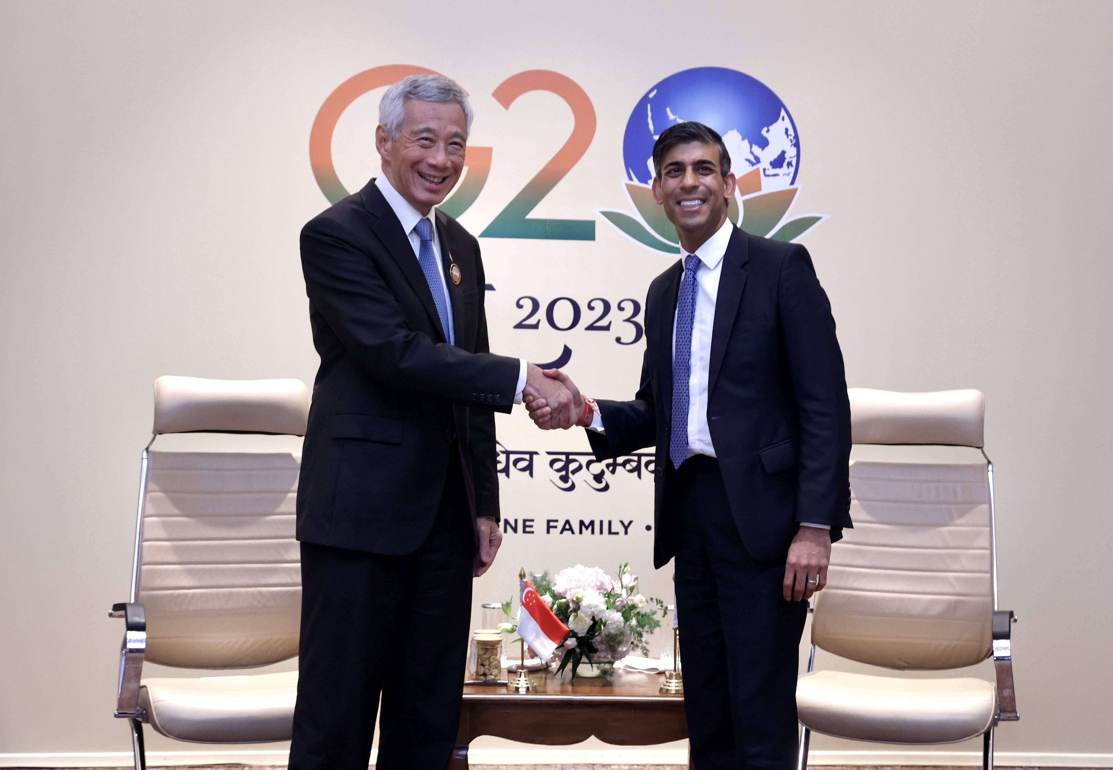 Lee Hsien Loong and Rishi Sunak shake hands in front of the G20 2023 logo.