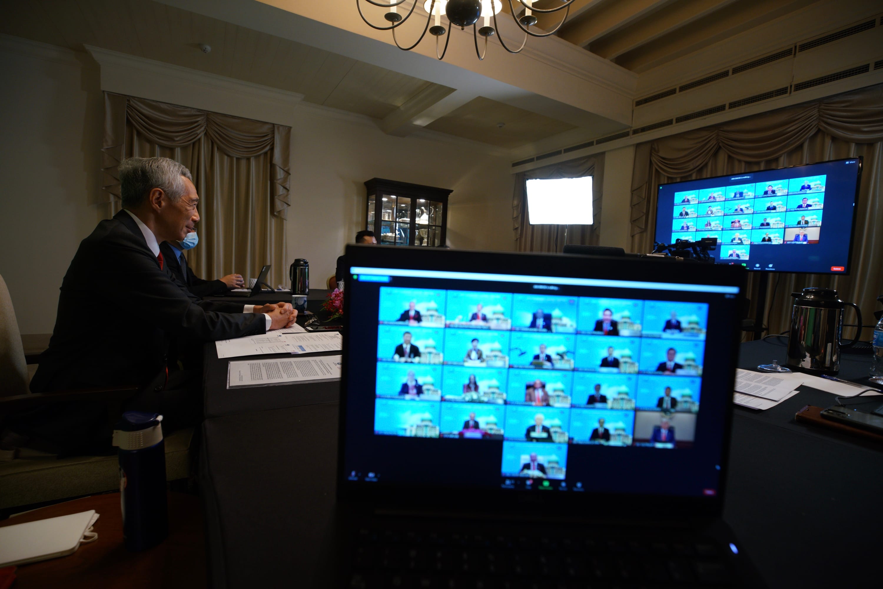 Conference room; PM Lee sits at a table with video conference displays.