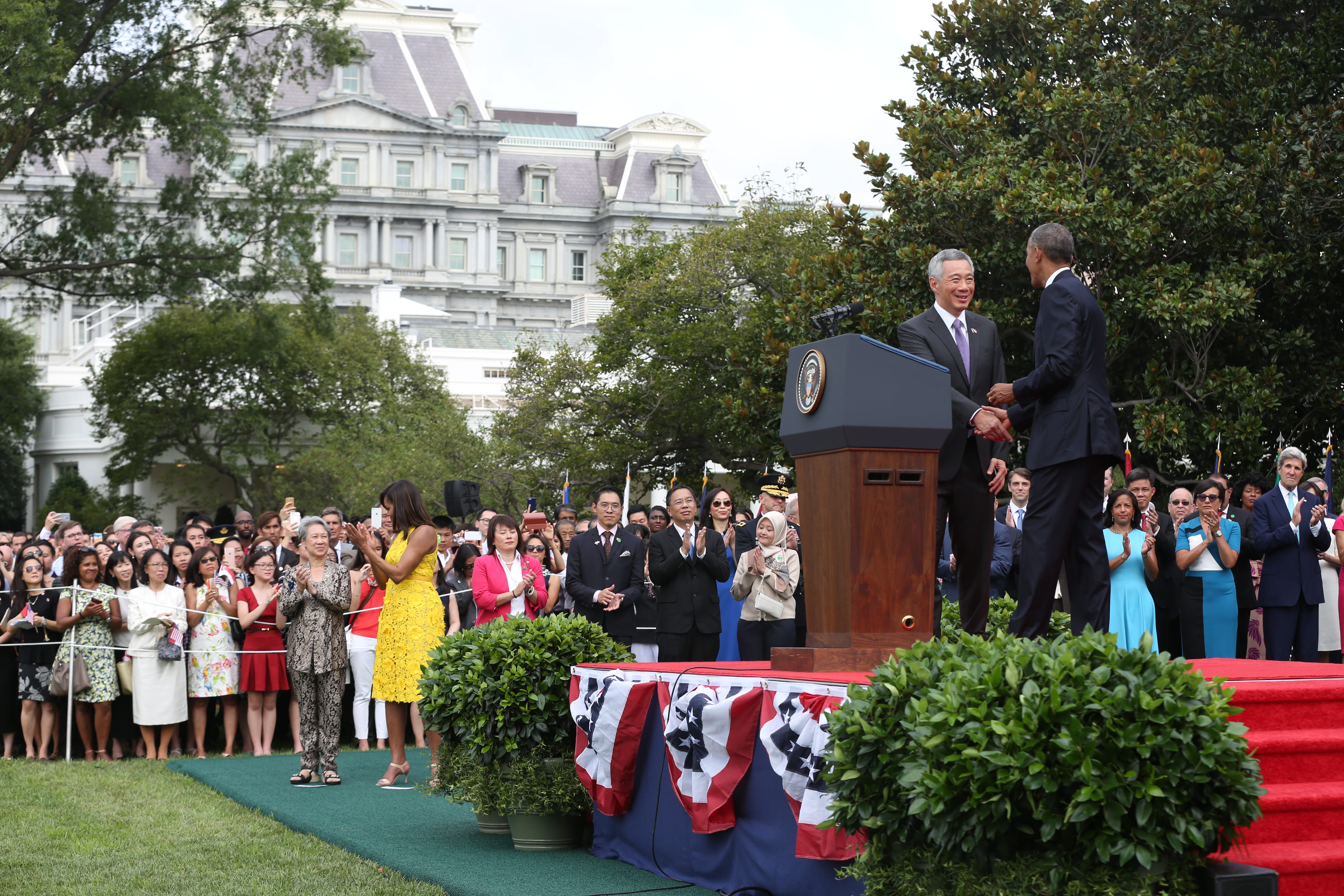 Obama and Lee Hsien Loong shake hands at podium before clapping crowd. White House in background.
