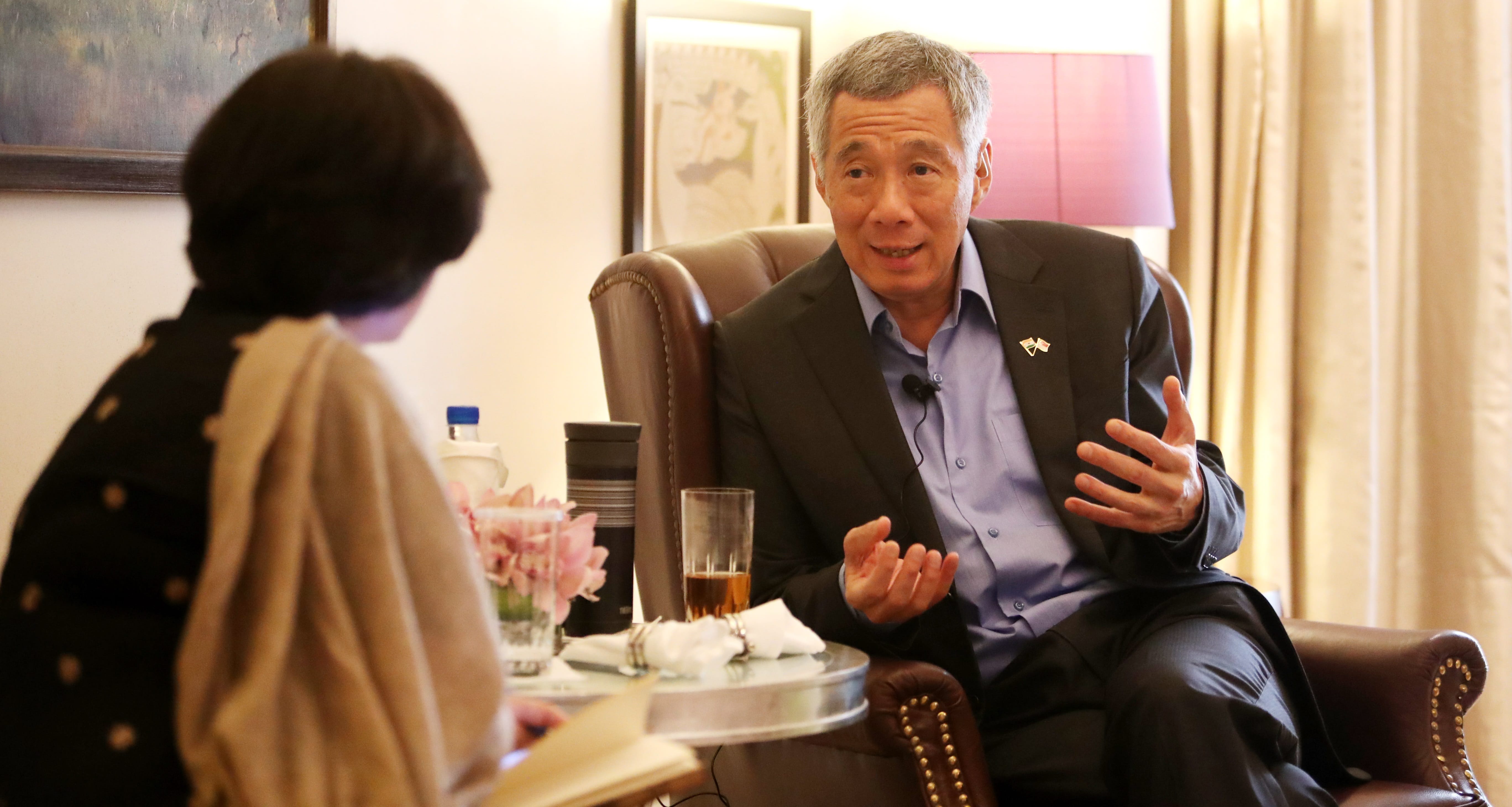 Lee Hsien Loong gestures during interview. Woman with notebook is visible.