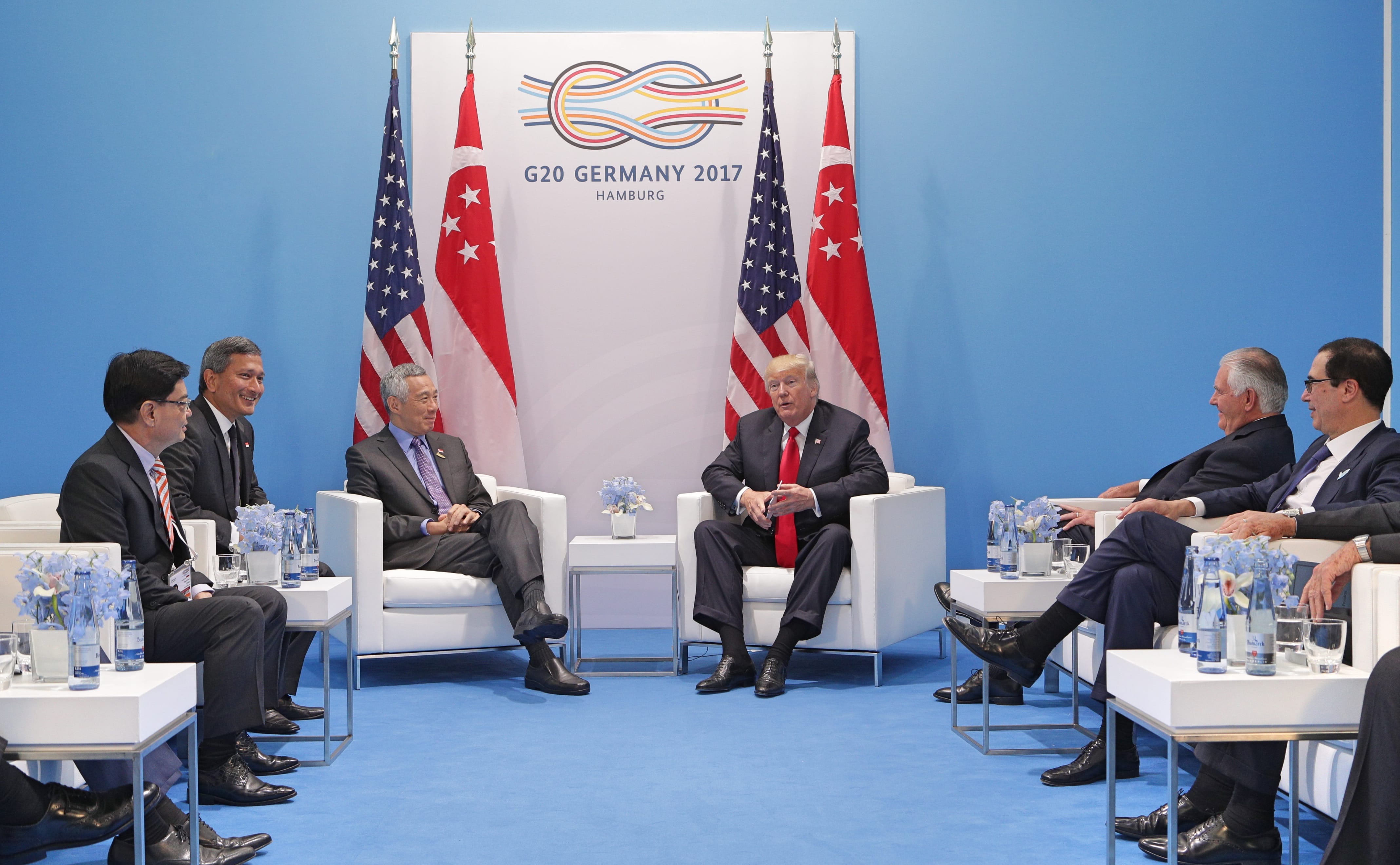 World leaders, including Trump, seated at the G20 summit in Germany, with flags and table decor.