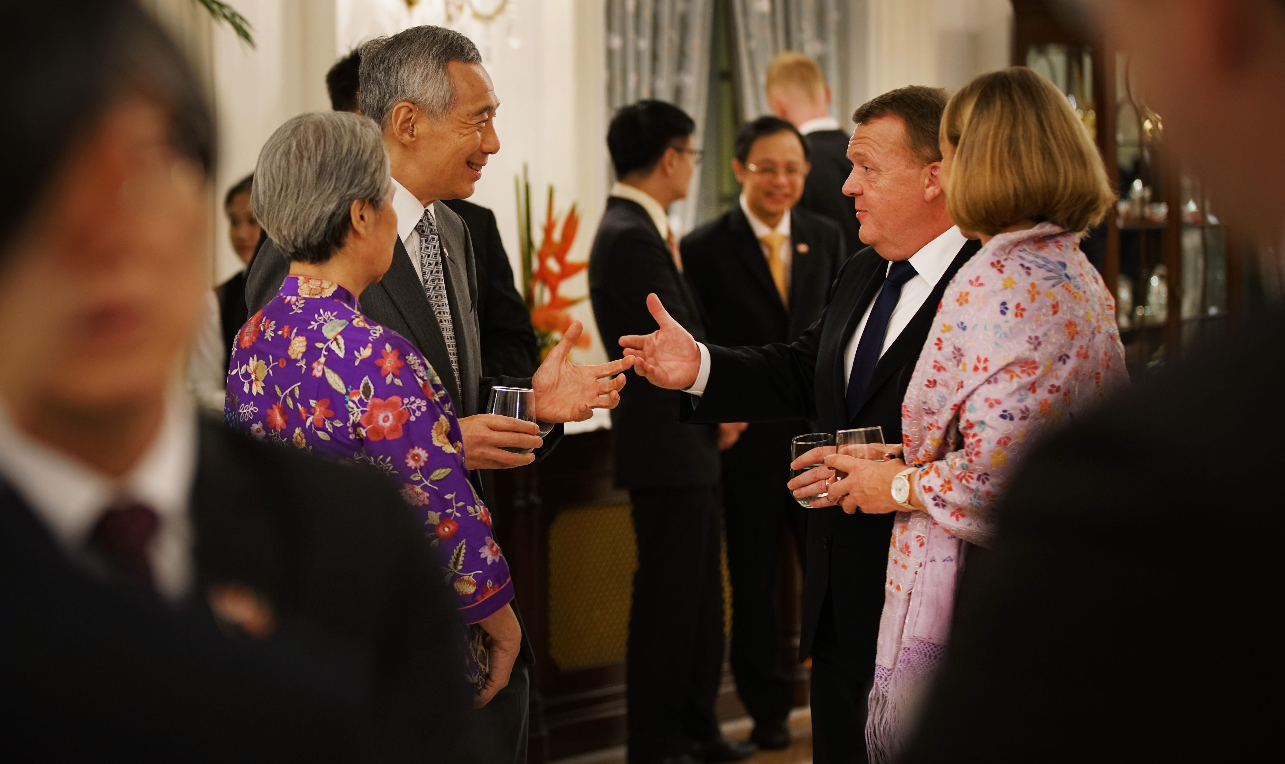 Lee Hsien Loong at a reception, gesturing with a glass, talking to guests.