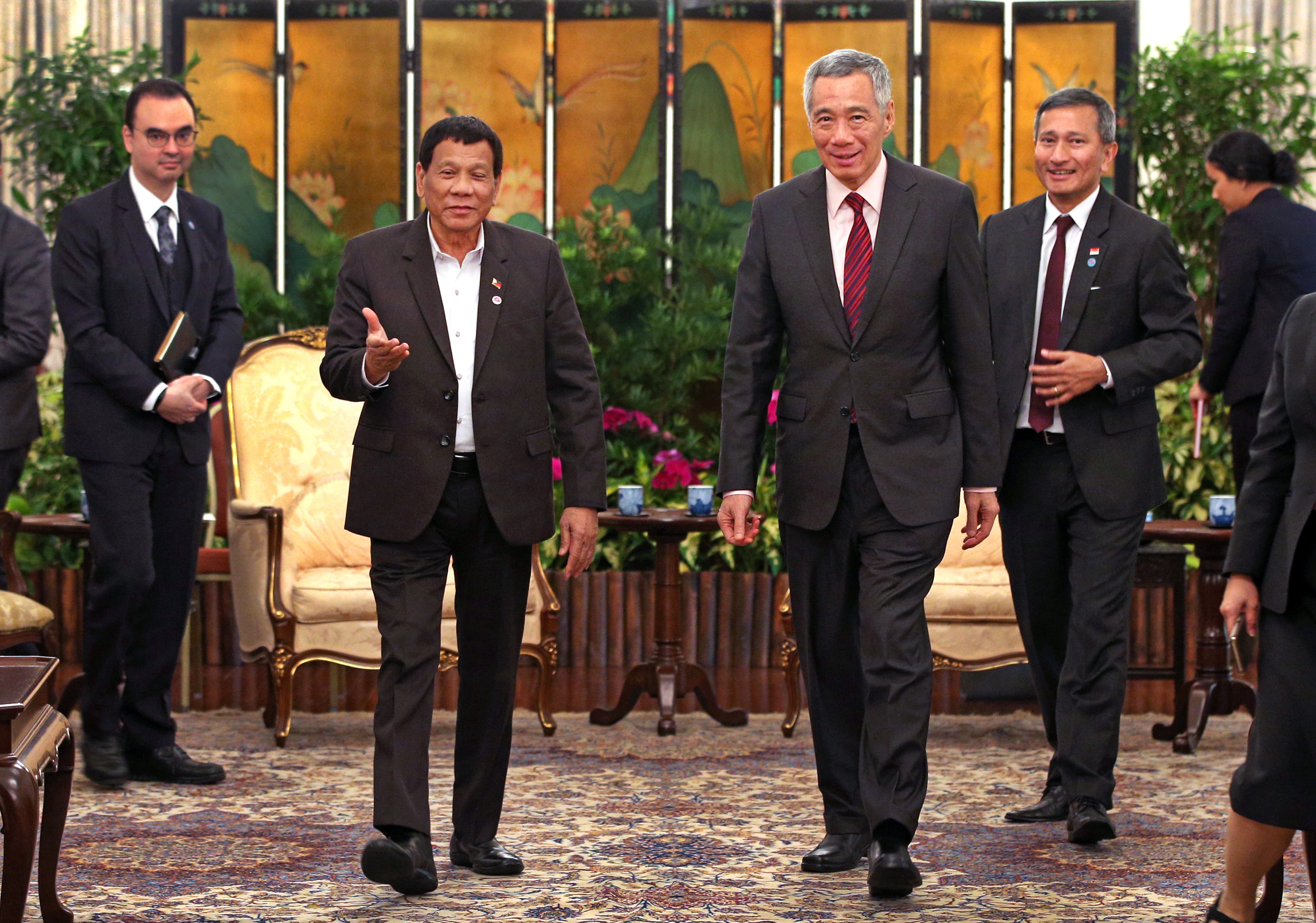 Rodrigo Duterte and Lee Hsien Loong walk in suits across patterned carpet, followed by other people.