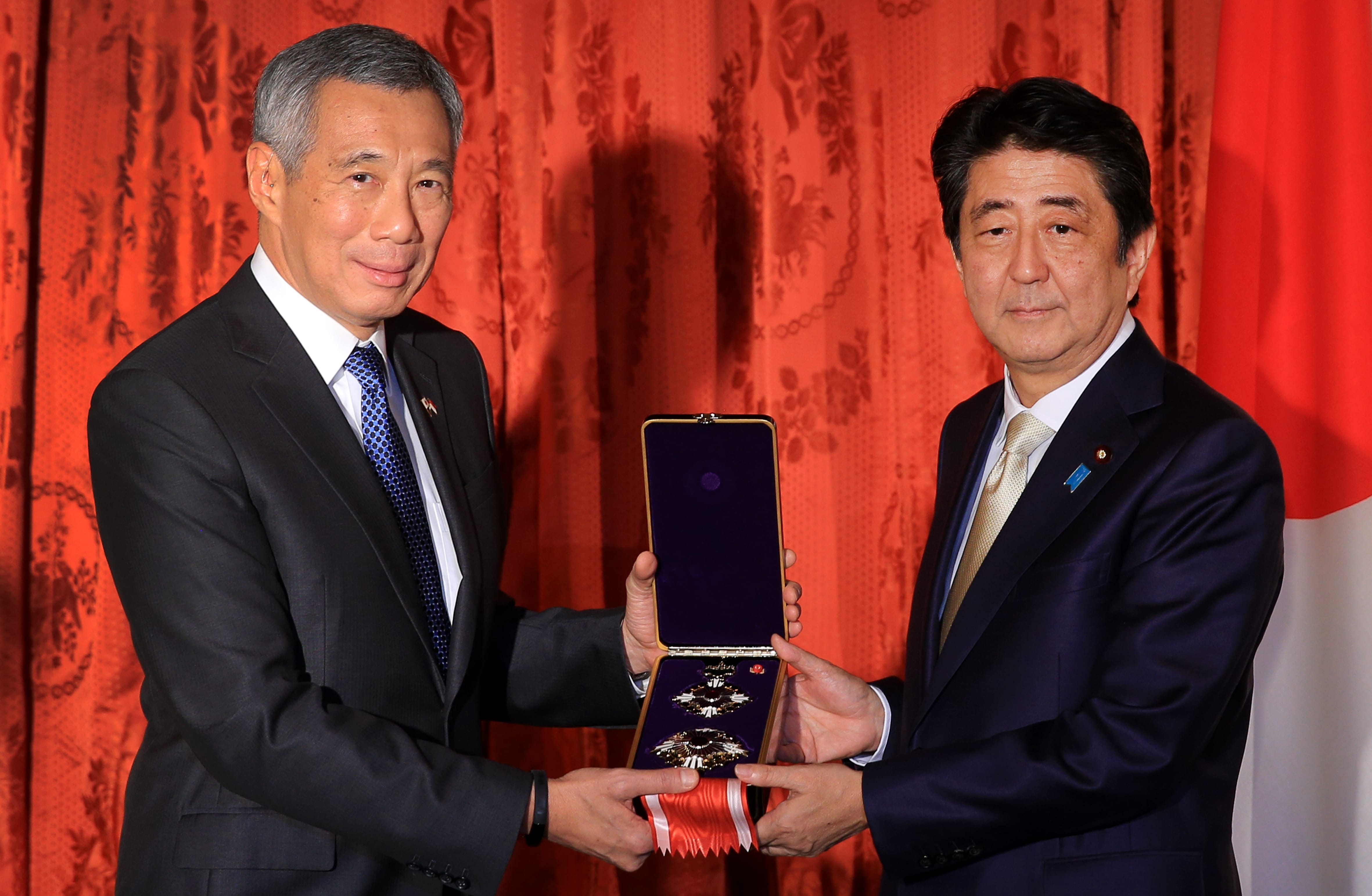 Lee Hsien Loong and Shinzo Abe holding a medal in an open case, in front of red curtains and a Japanese flag.