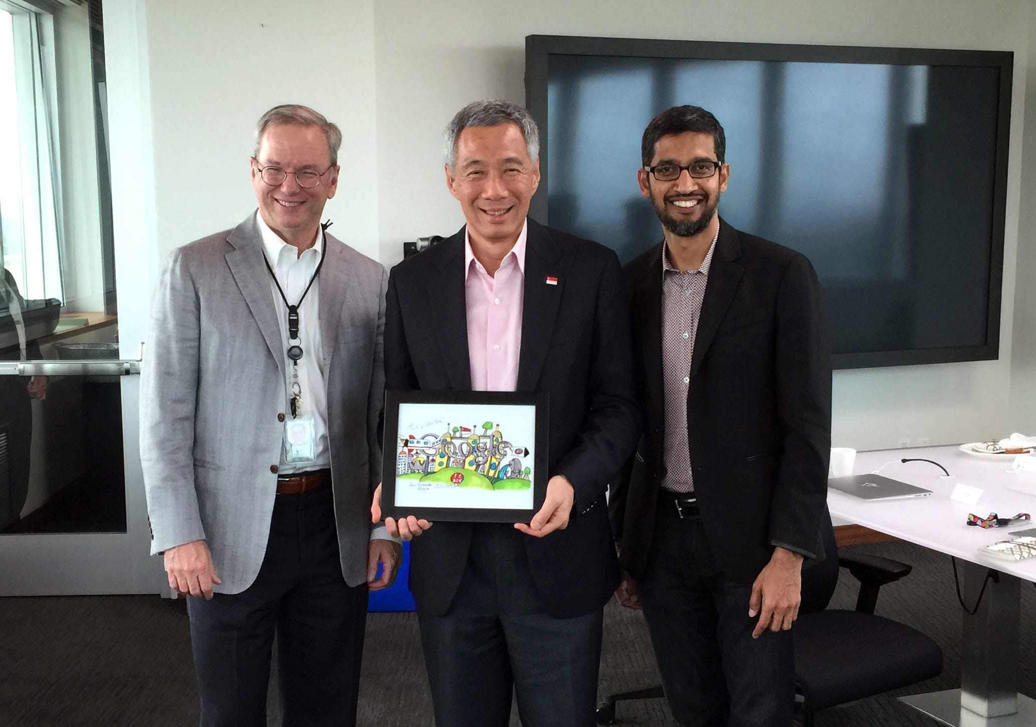 Three men pose indoors, one holding framed artwork. Google CEO Sundar Pichai on right.