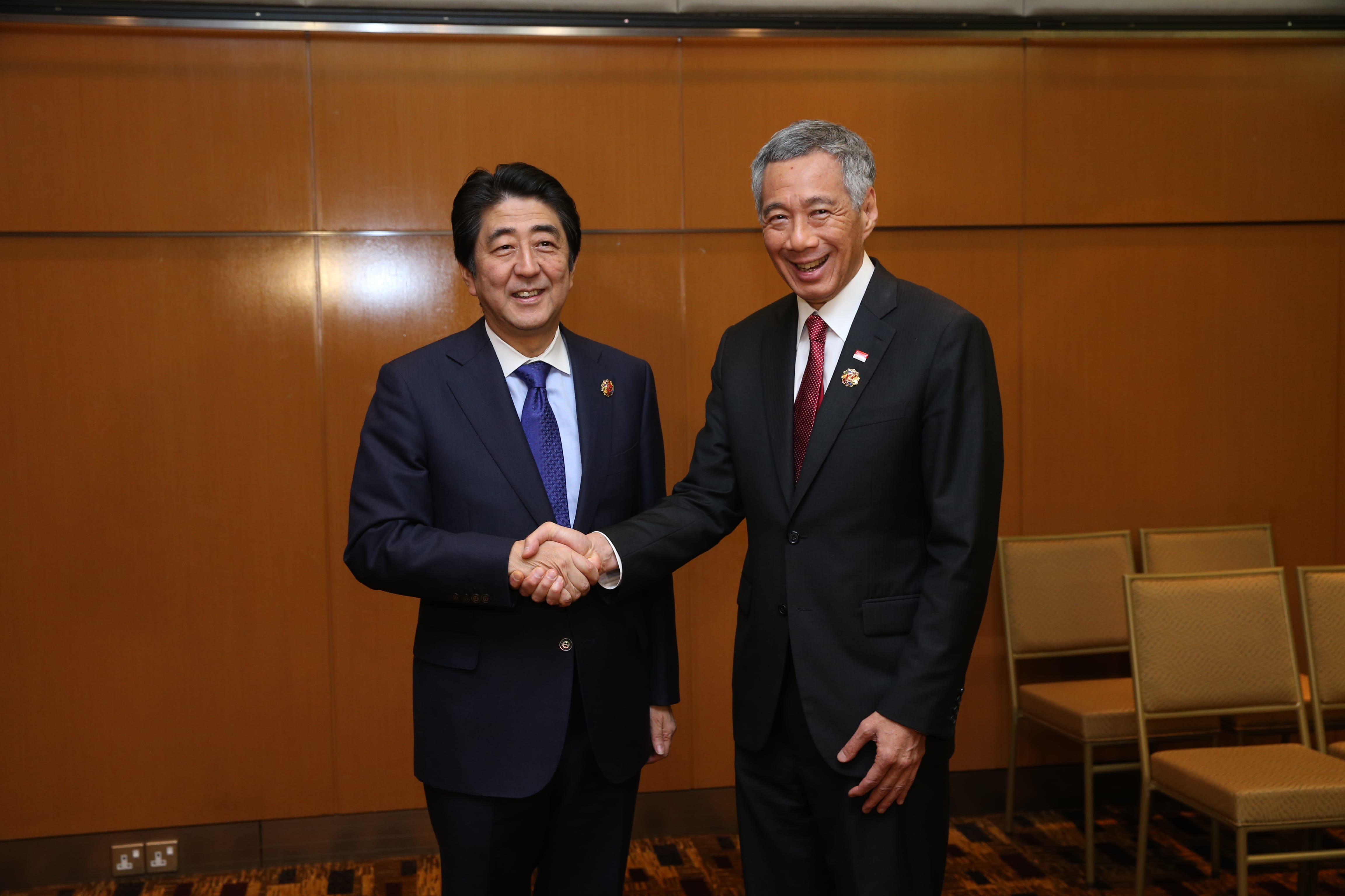 Shinzo Abe and Lee Hsien Loong in suits shaking hands, smiling.