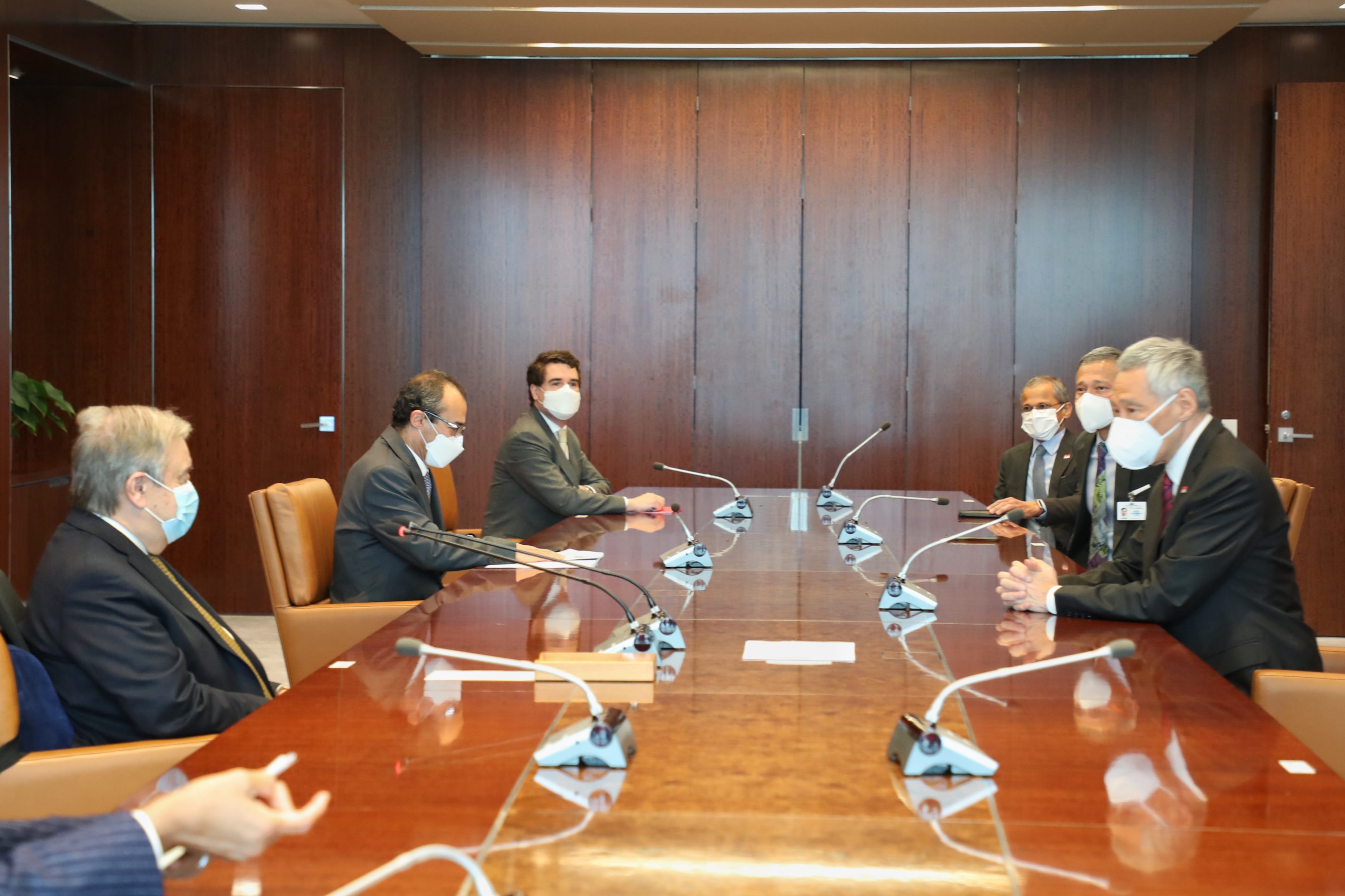People in suits wearing masks at a conference table with microphones.