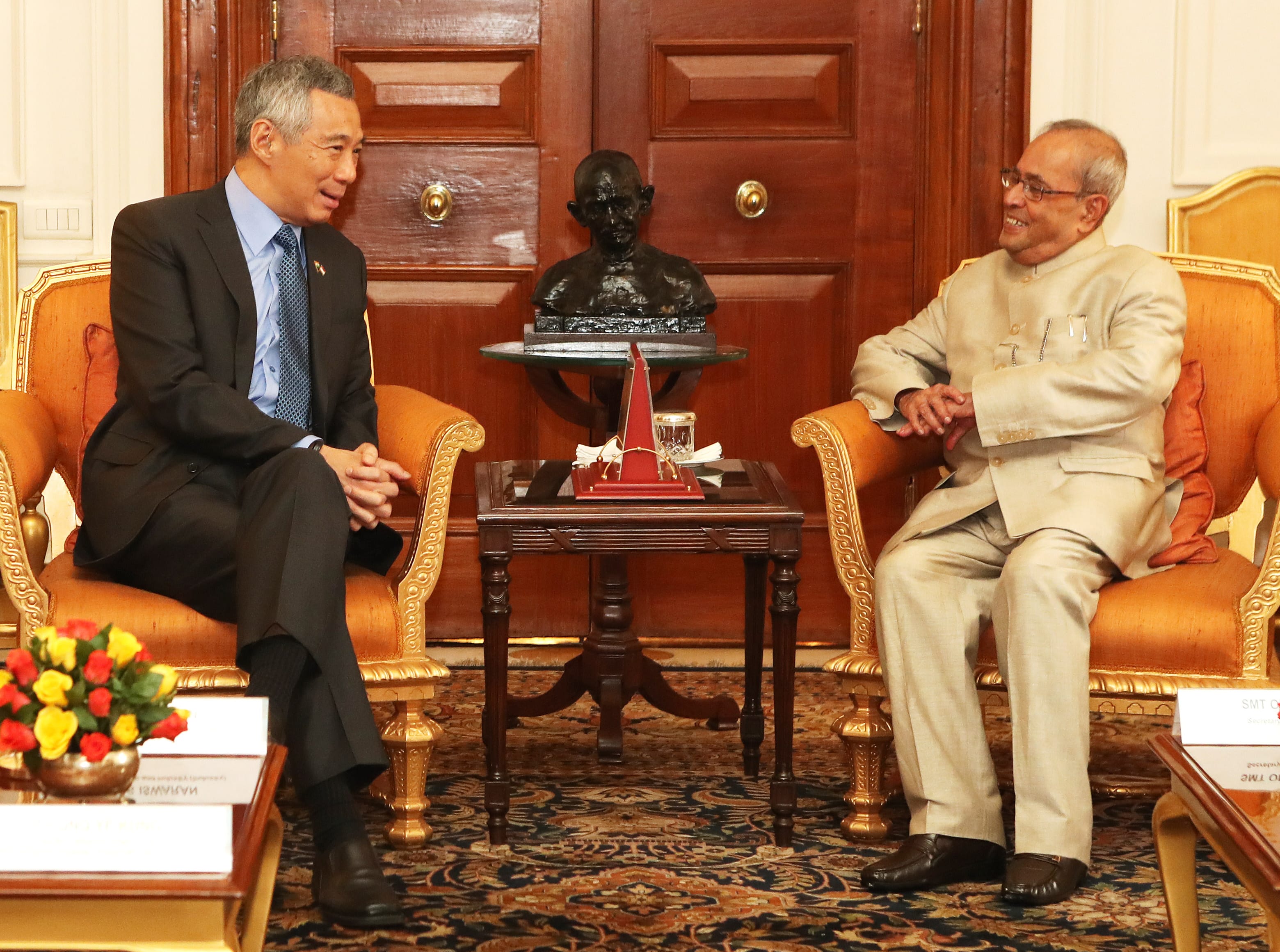 Two men, Lee Hsien Loong and Pranab Mukherjee, sit in ornate chairs with a bust of Gandhi between them.