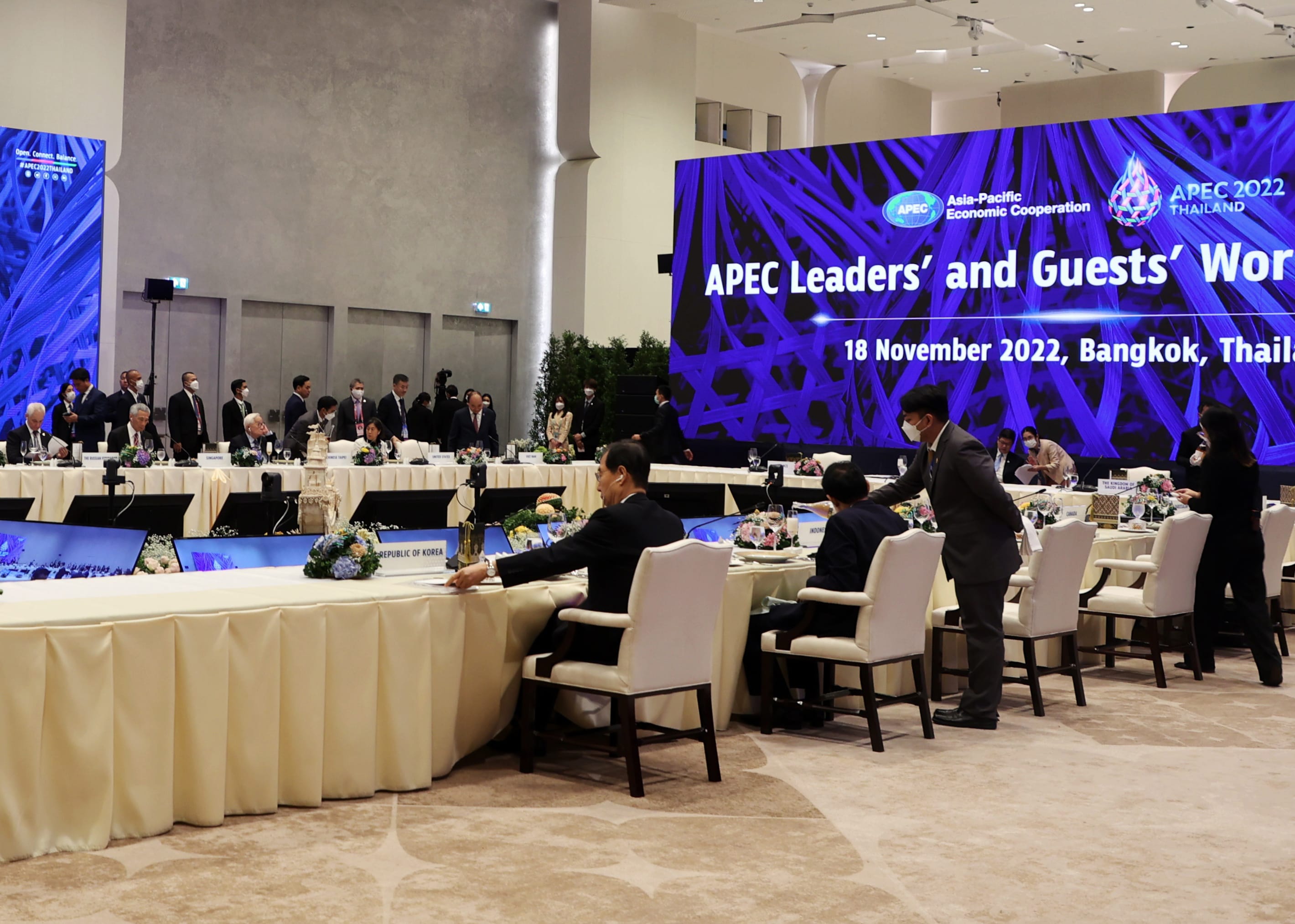 APEC 2022 Thailand meeting; officials seated at tables in a conference room, large screen with event logo.