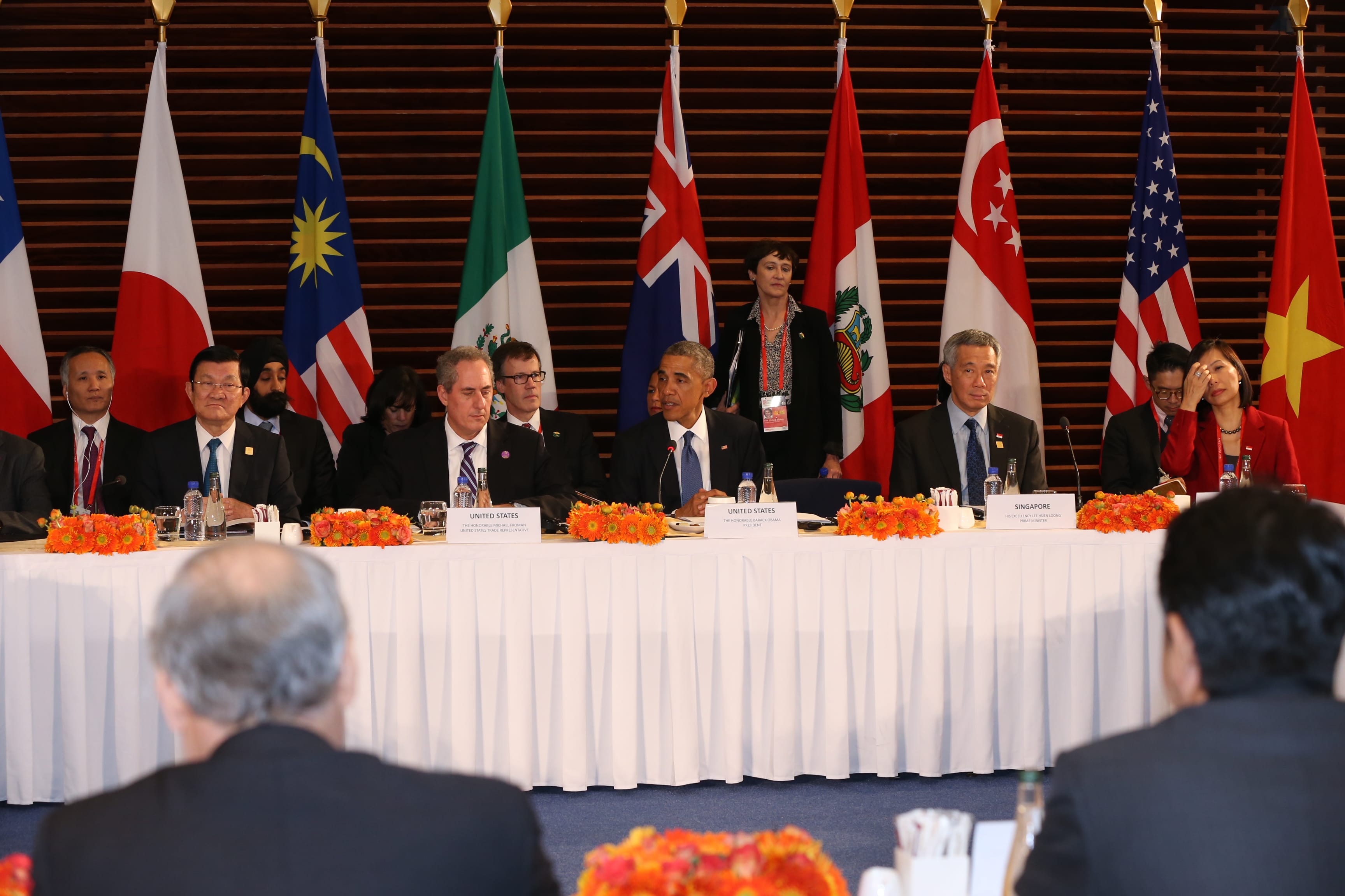 Leaders at a long table with flags, including the USA flag and Barack Obama.