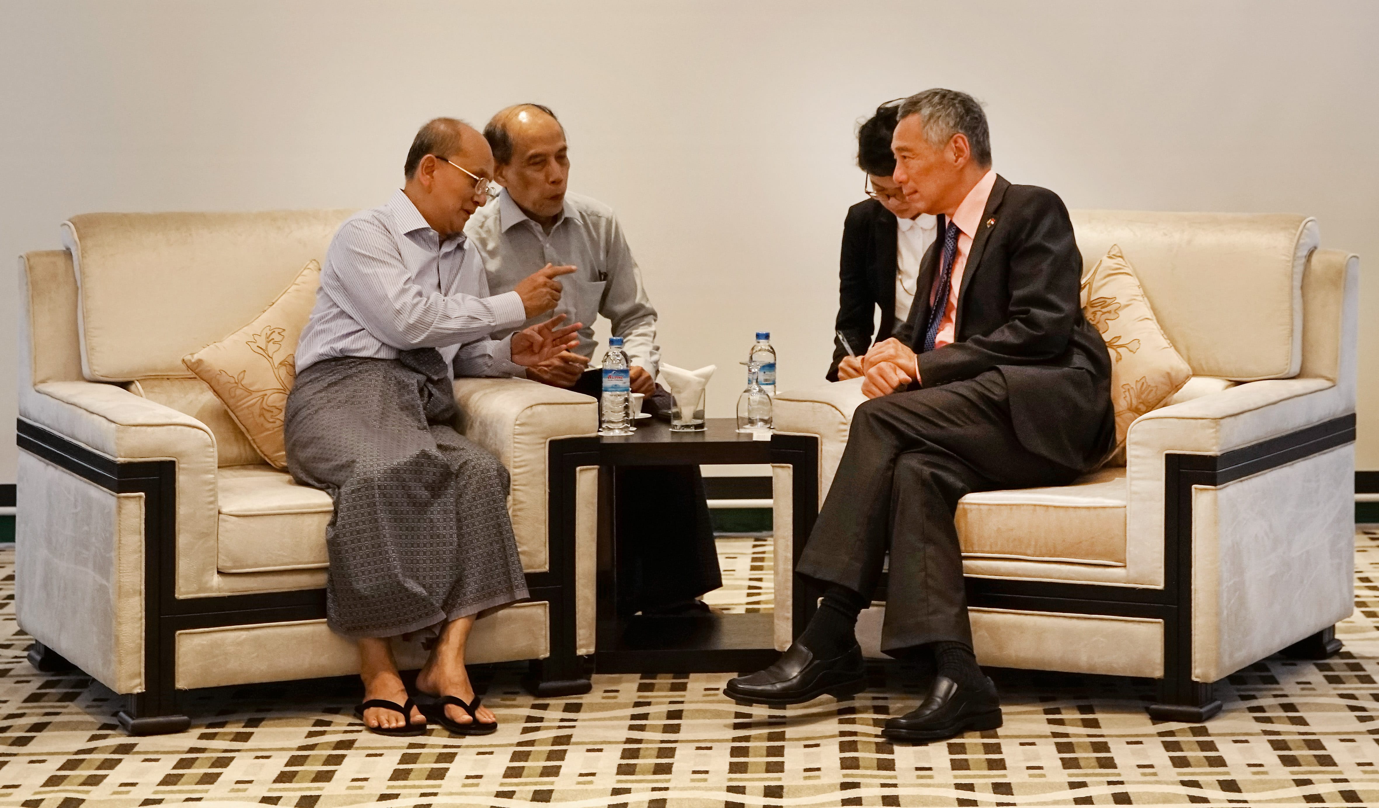 Lee Hsien Loong sits on a couch talking with two men, another woman standing behind.