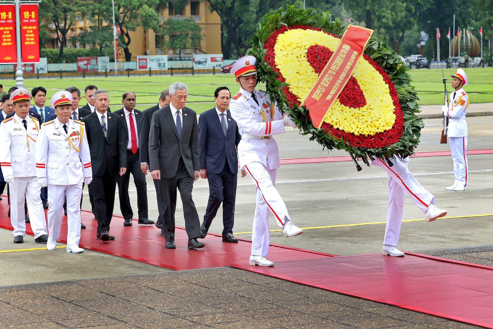 Formal procession: Lee Hsien Loong walks with guards carrying a floral wreath on a red carpet.