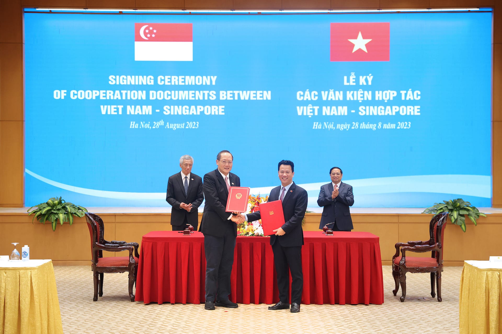 Signing ceremony of cooperation documents between Vietnam and Singapore with flags. Two men shaking hands.