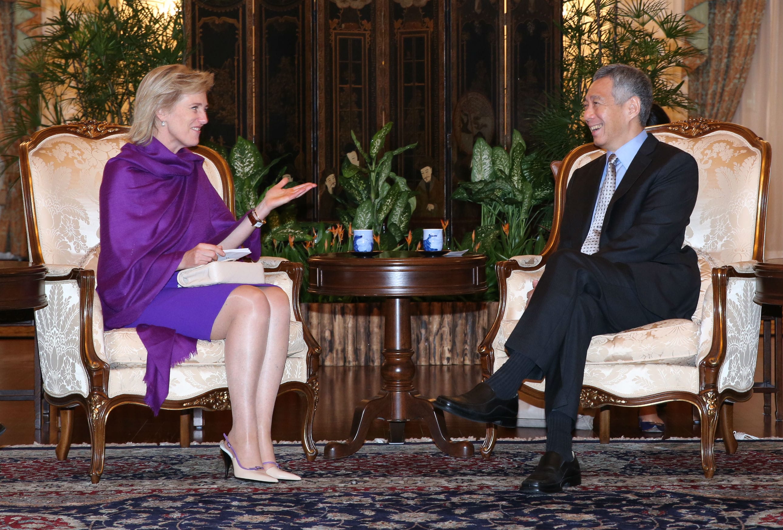 Woman with purple shawl and Lee Hsien Loong sit in ornate chairs, facing each other.