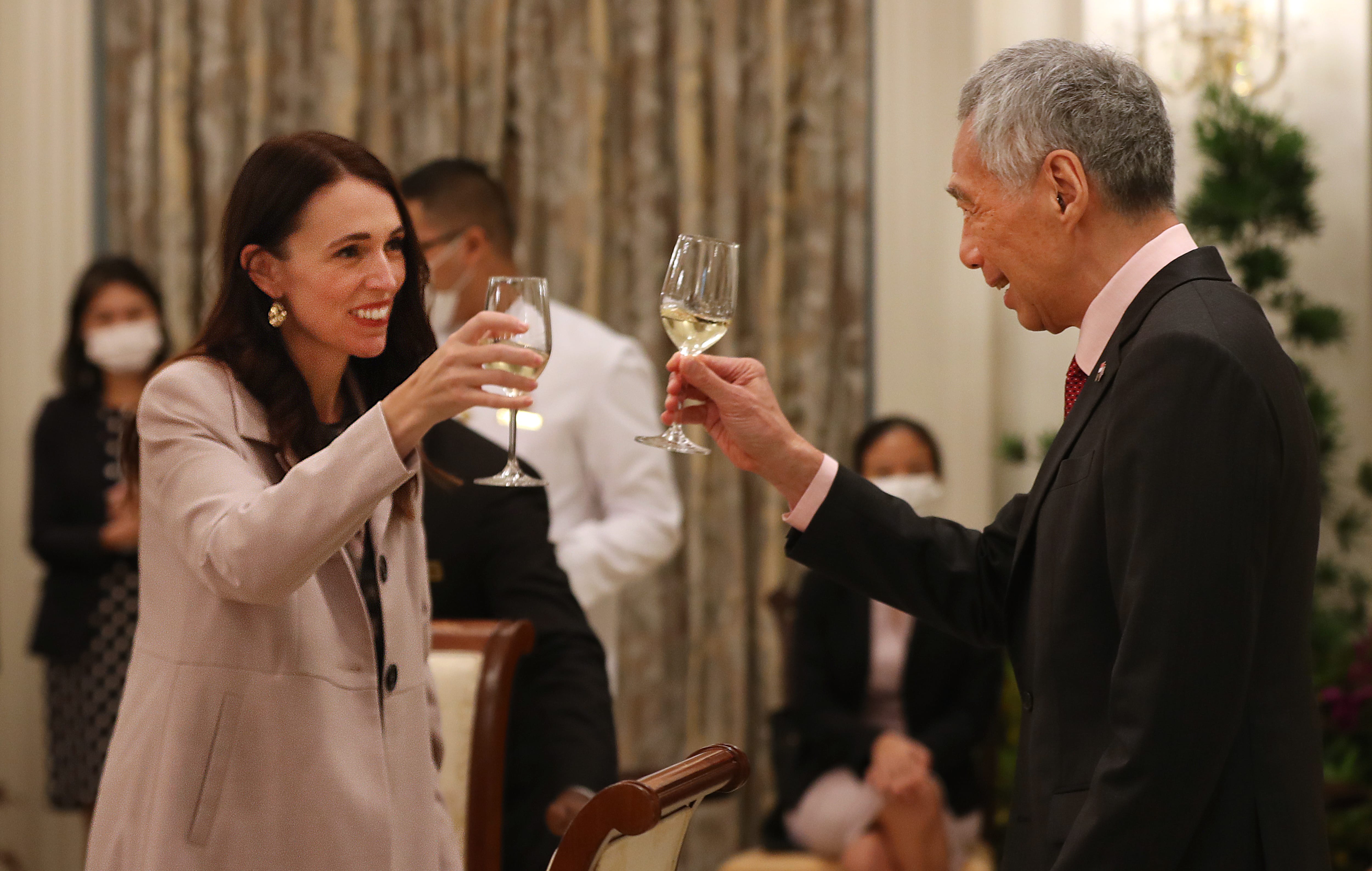 Jacinda Ardern and Lee Hsien Loong toast with wine glasses at an event.