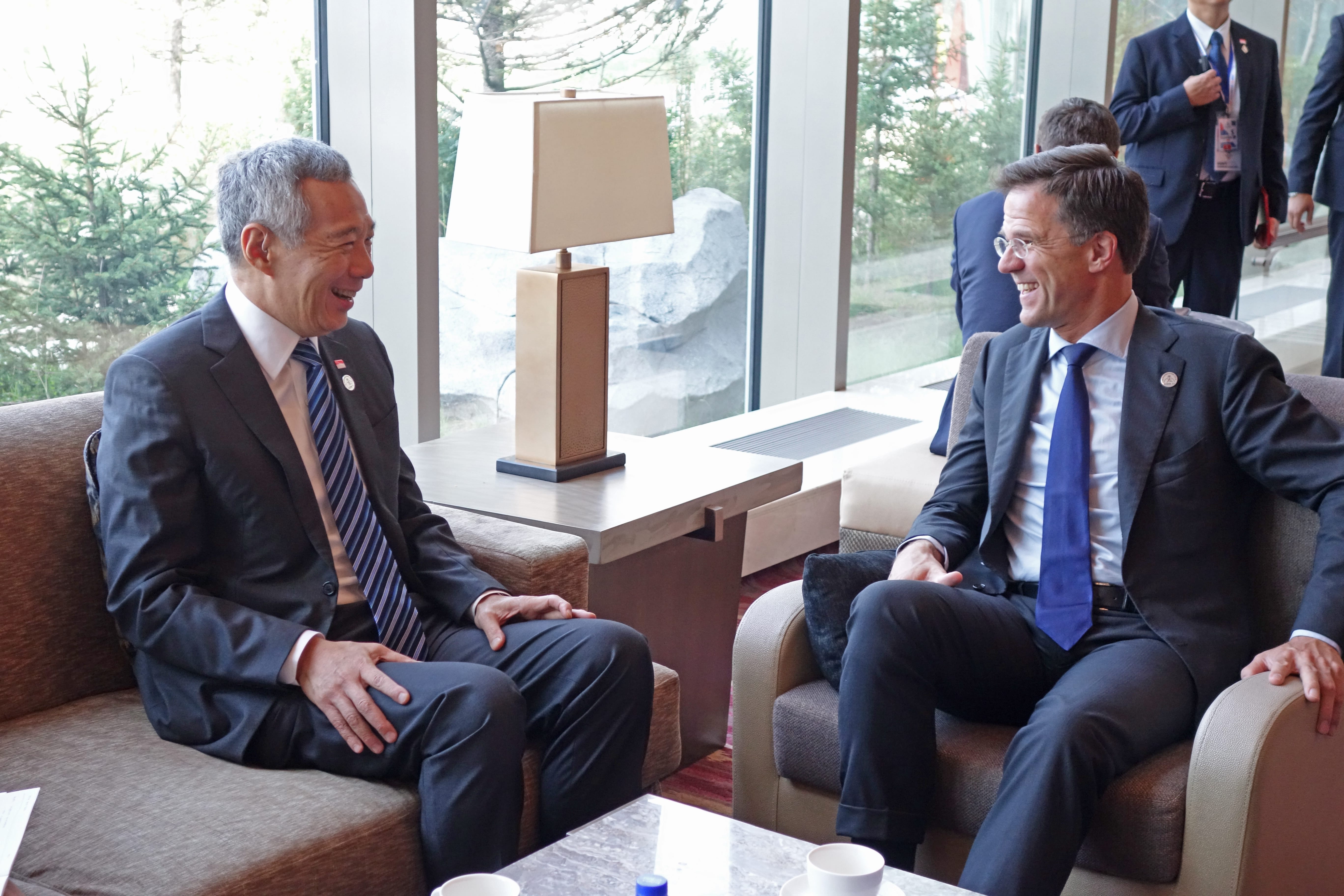 Lee Hsien Loong and Mark Rutte in suits, sitting and talking in a lounge.