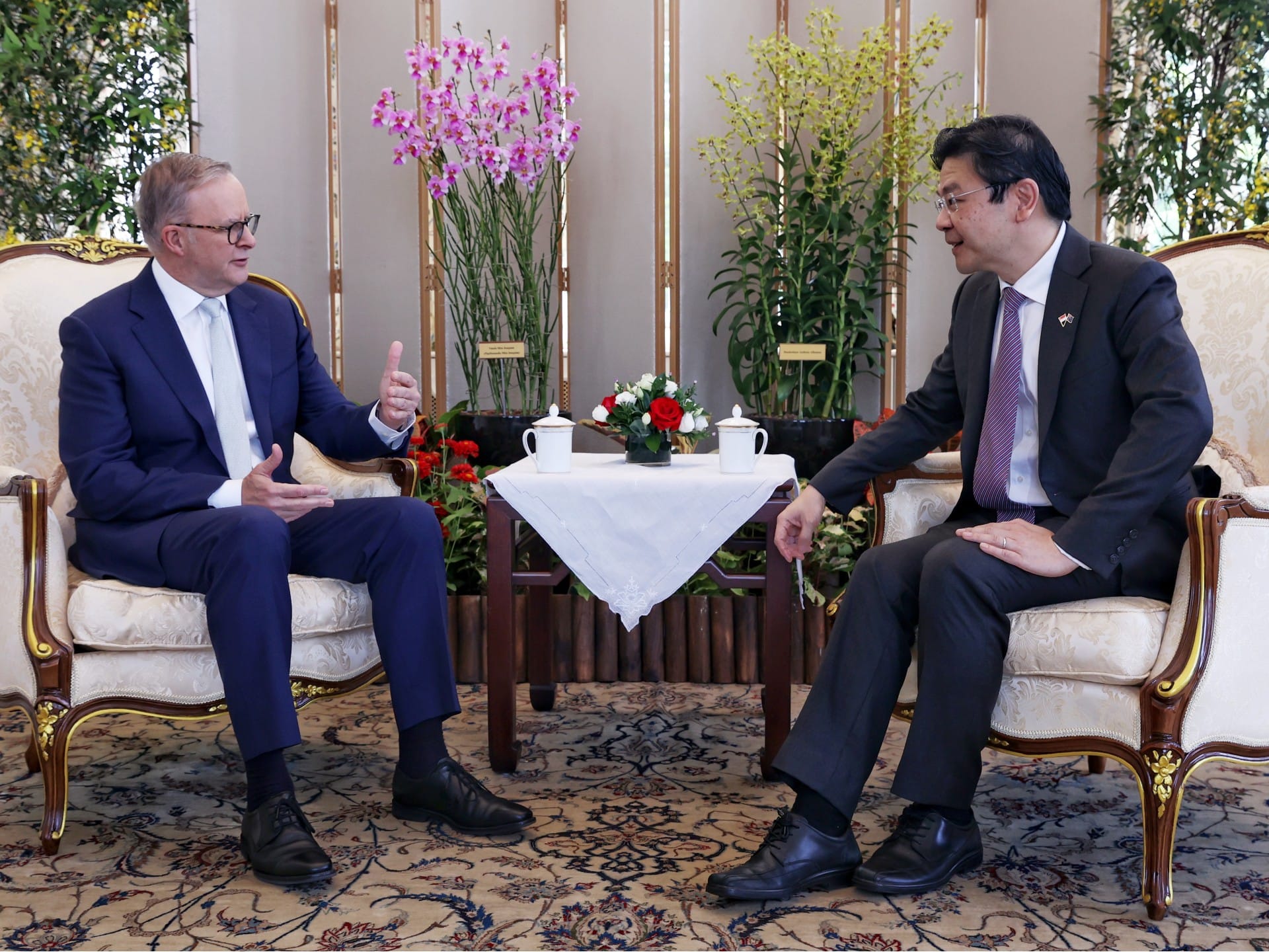 Two men in suits sit facing each other having a discussion indoors.