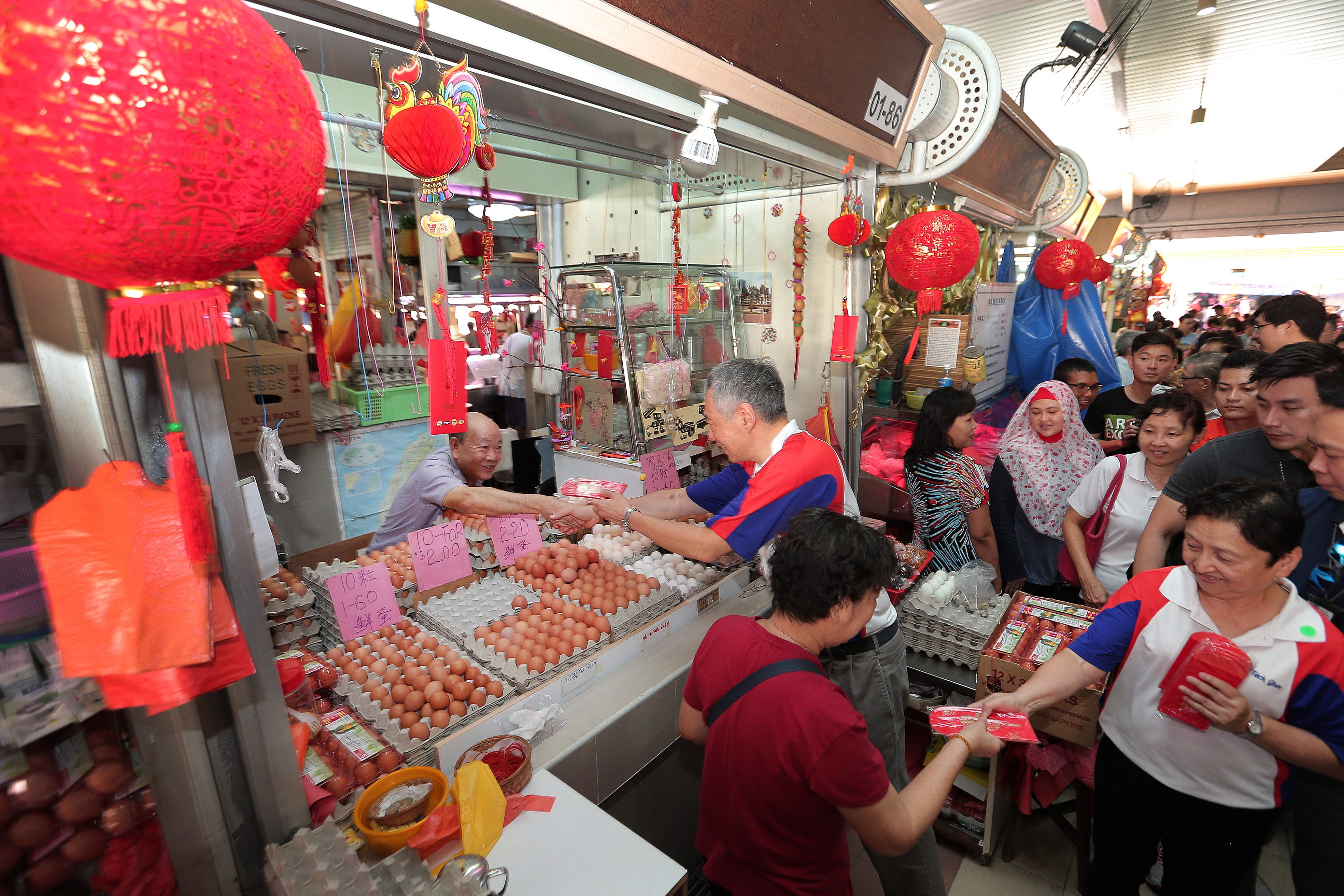 Crowded market stall selling eggs, red lanterns hanging. People exchanging money and red envelopes.