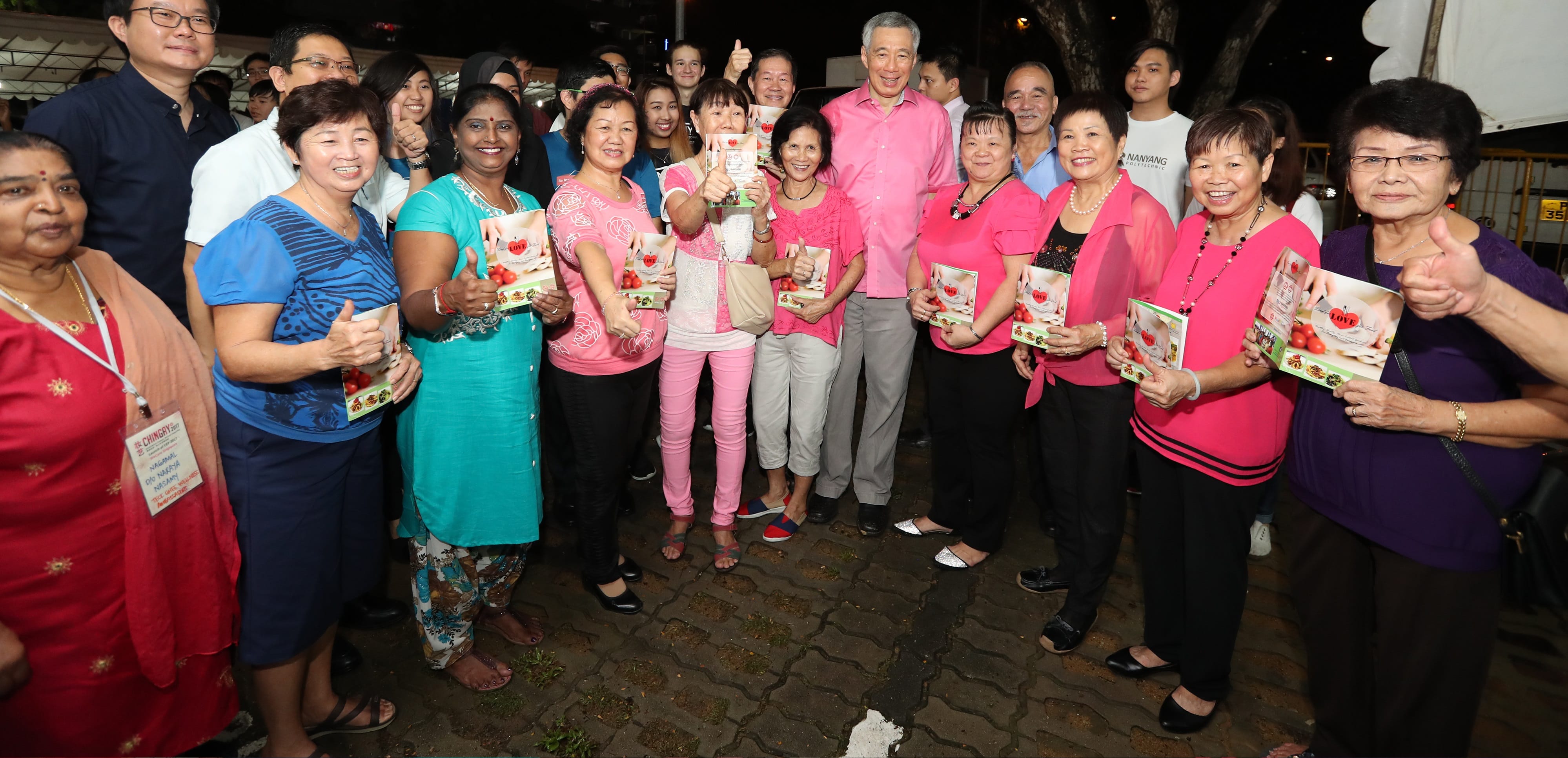 Group of people giving thumbs up, holding 'Love' cookbooks; Lee Hsien Loong is in pink shirt.