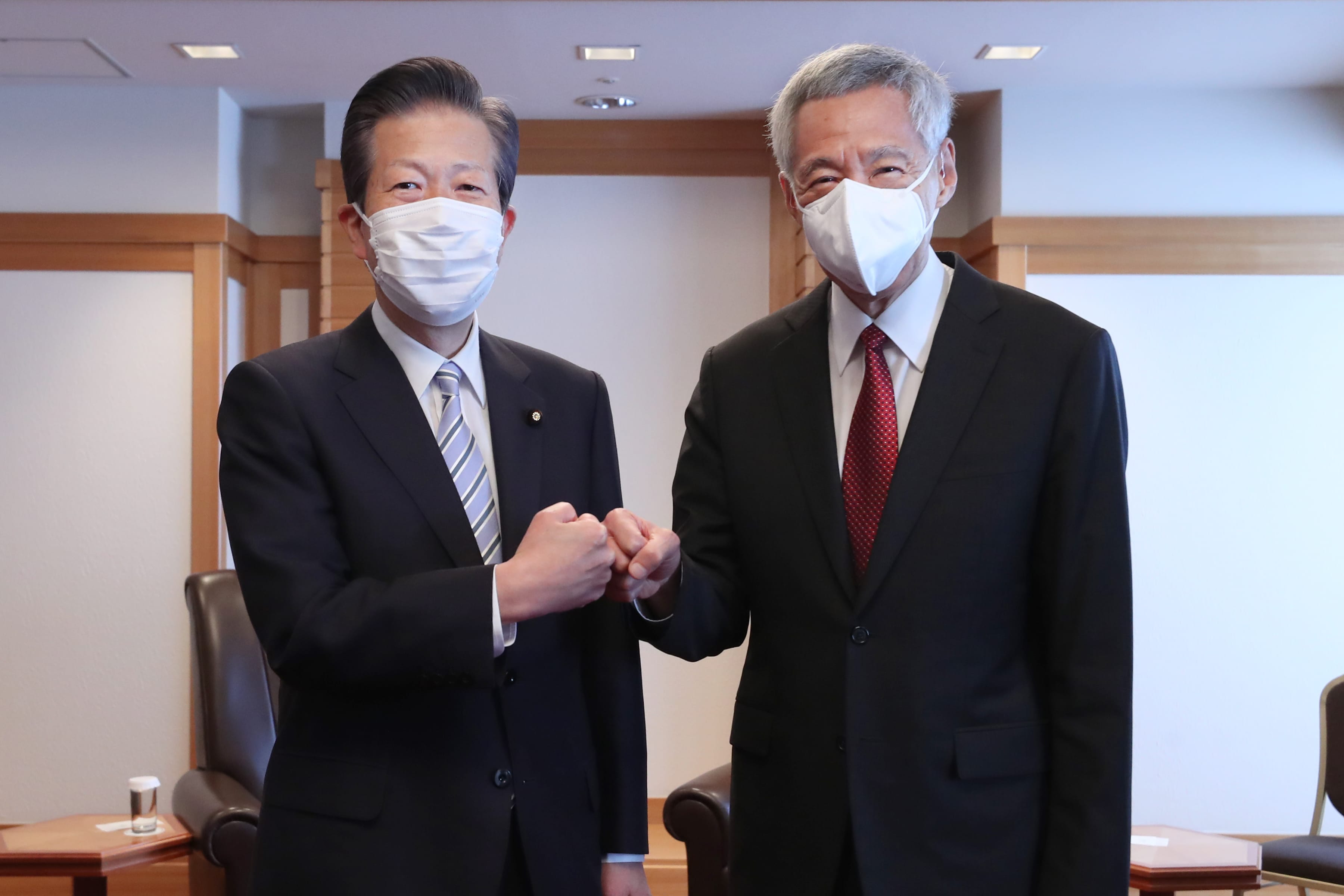 Two men in suits, wearing face masks, bump fists. Lee Hsien Loong on the right.