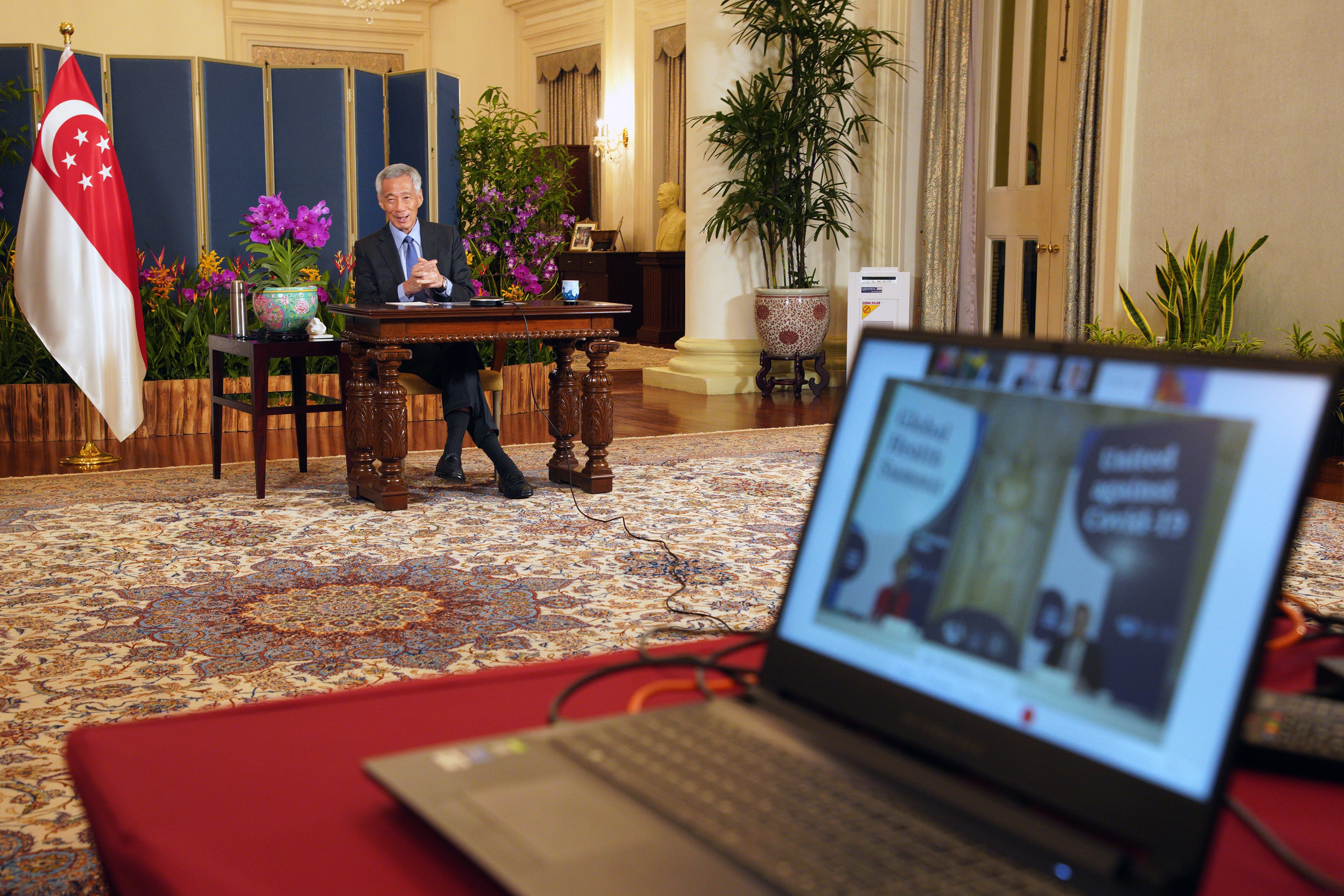 Lee Hsien Loong at a desk with the Singapore flag, seen through a laptop screen.