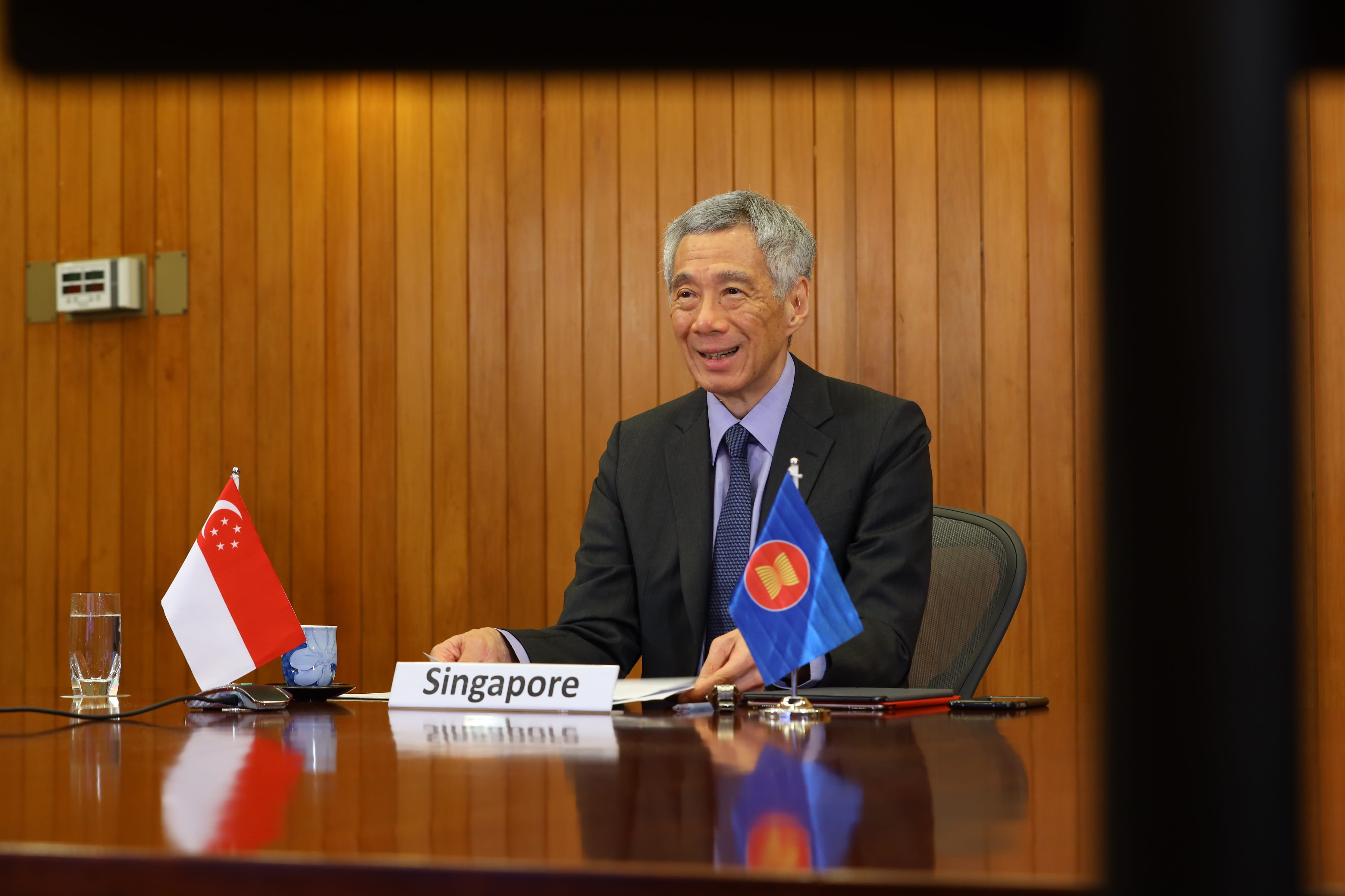 Lee Hsien Loong at table with flags of Singapore and ASEAN. Wood panel wall.