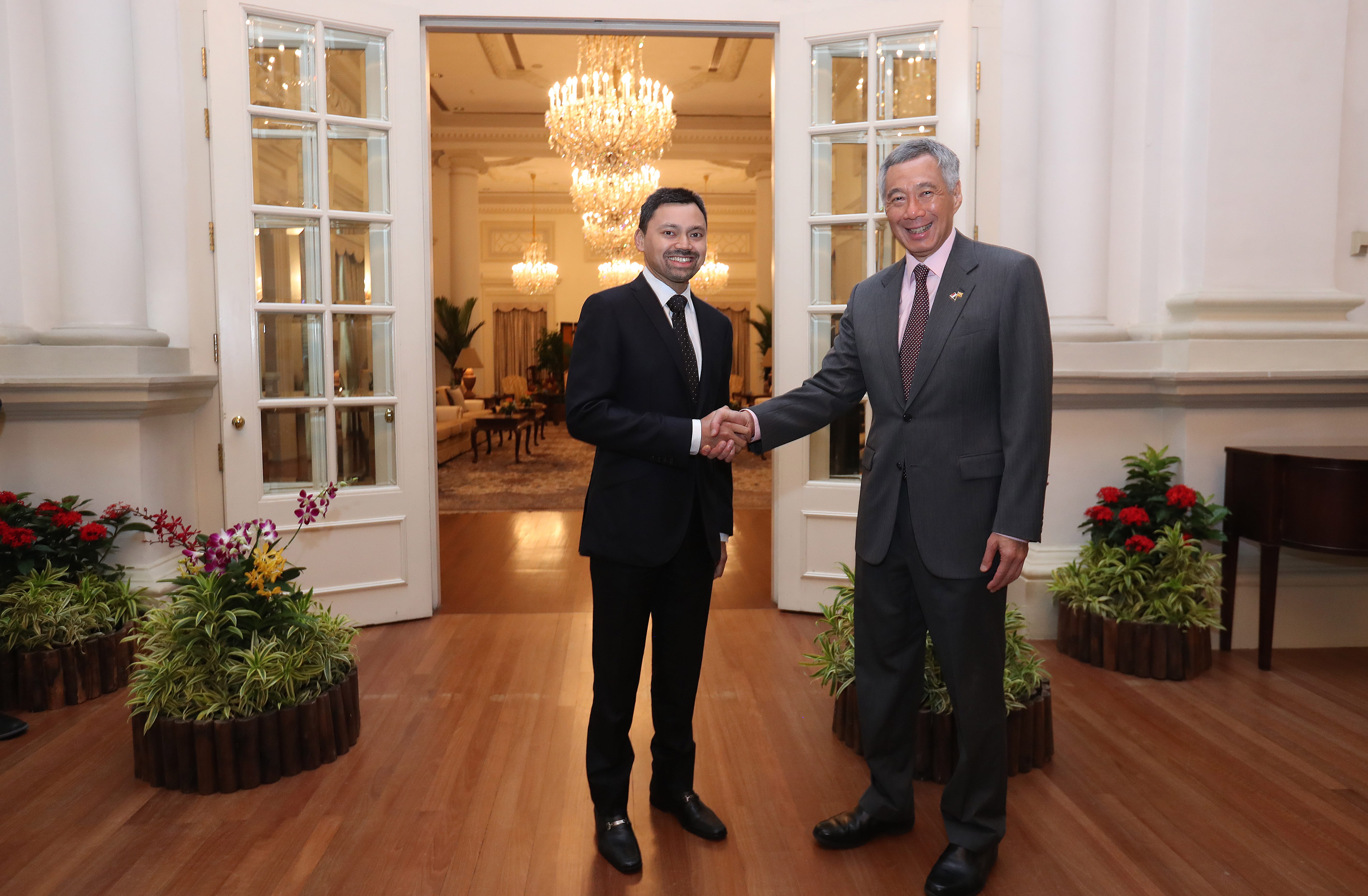 Two men in suits shake hands in front of open doorway. Lee Hsien Loong is on the right.
