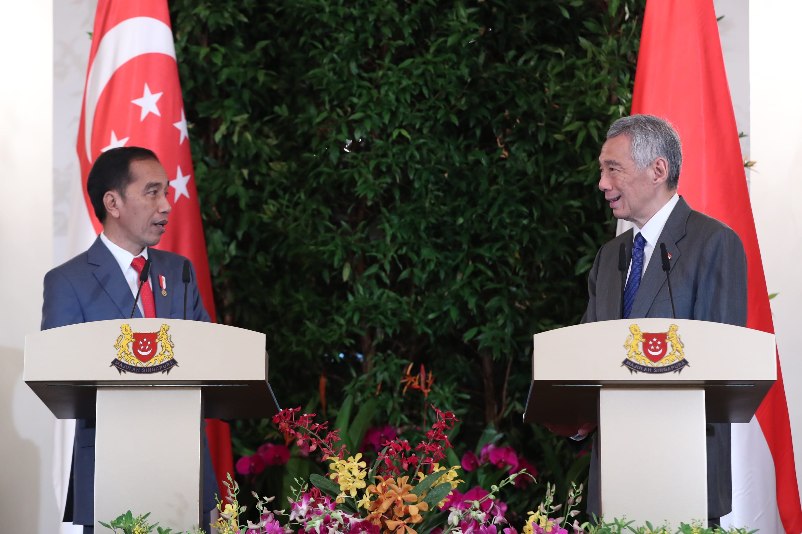 Jokowi and Lee Hsien Loong at podiums with Singapore flags and floral arrangements.