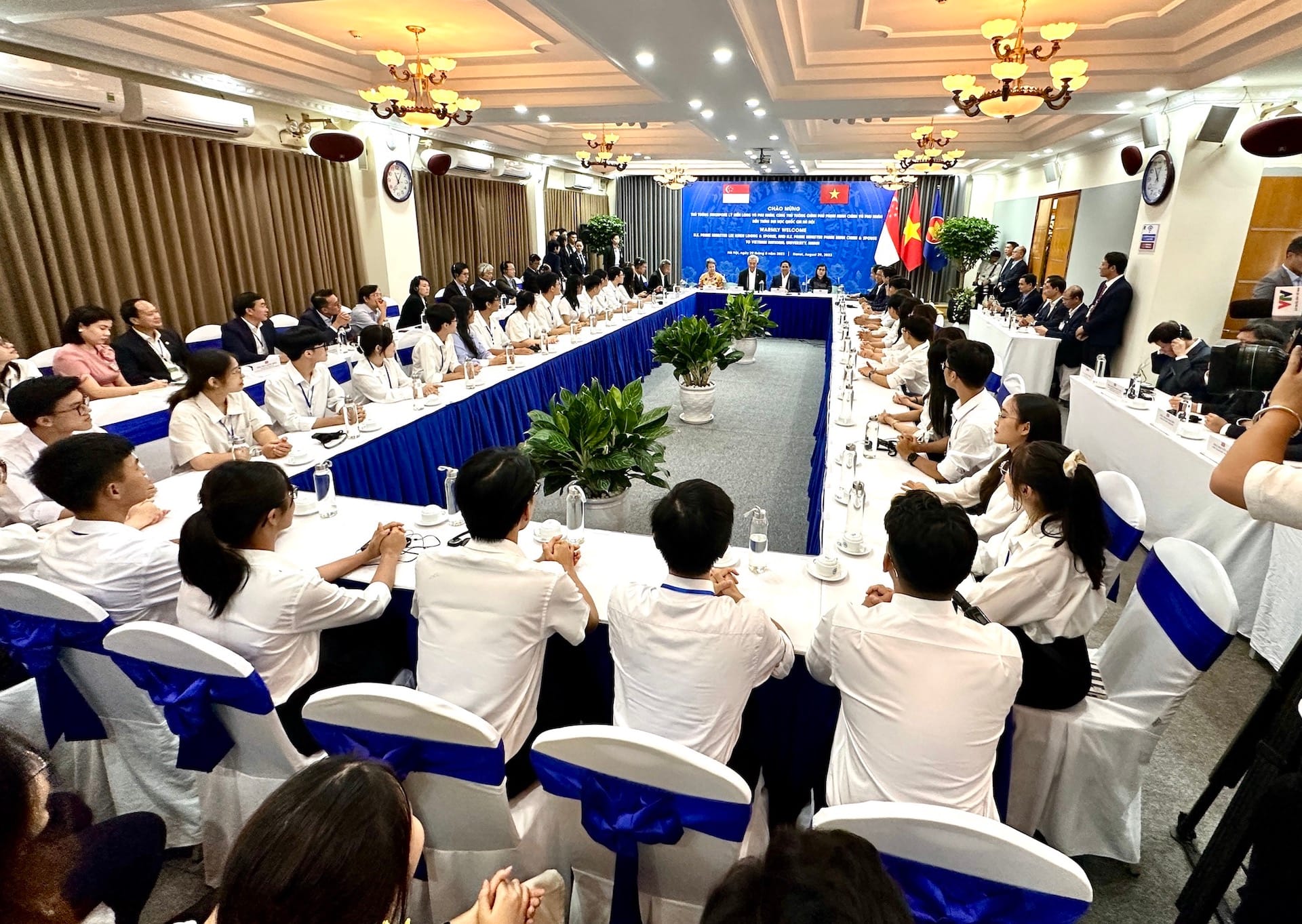 Meeting room with long tables of people in white shirts facing leaders under Vietnamese, Chinese flags.